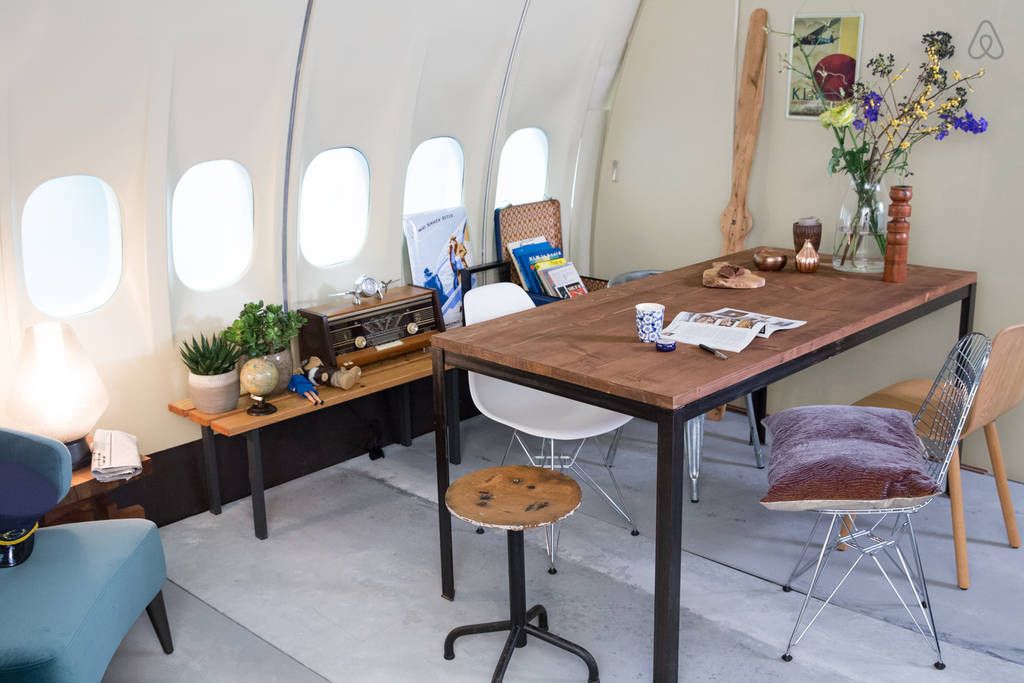 Interior view of an airplane converted into lodging, featuring a dining area with a wooden table, vintage radio, and plants.