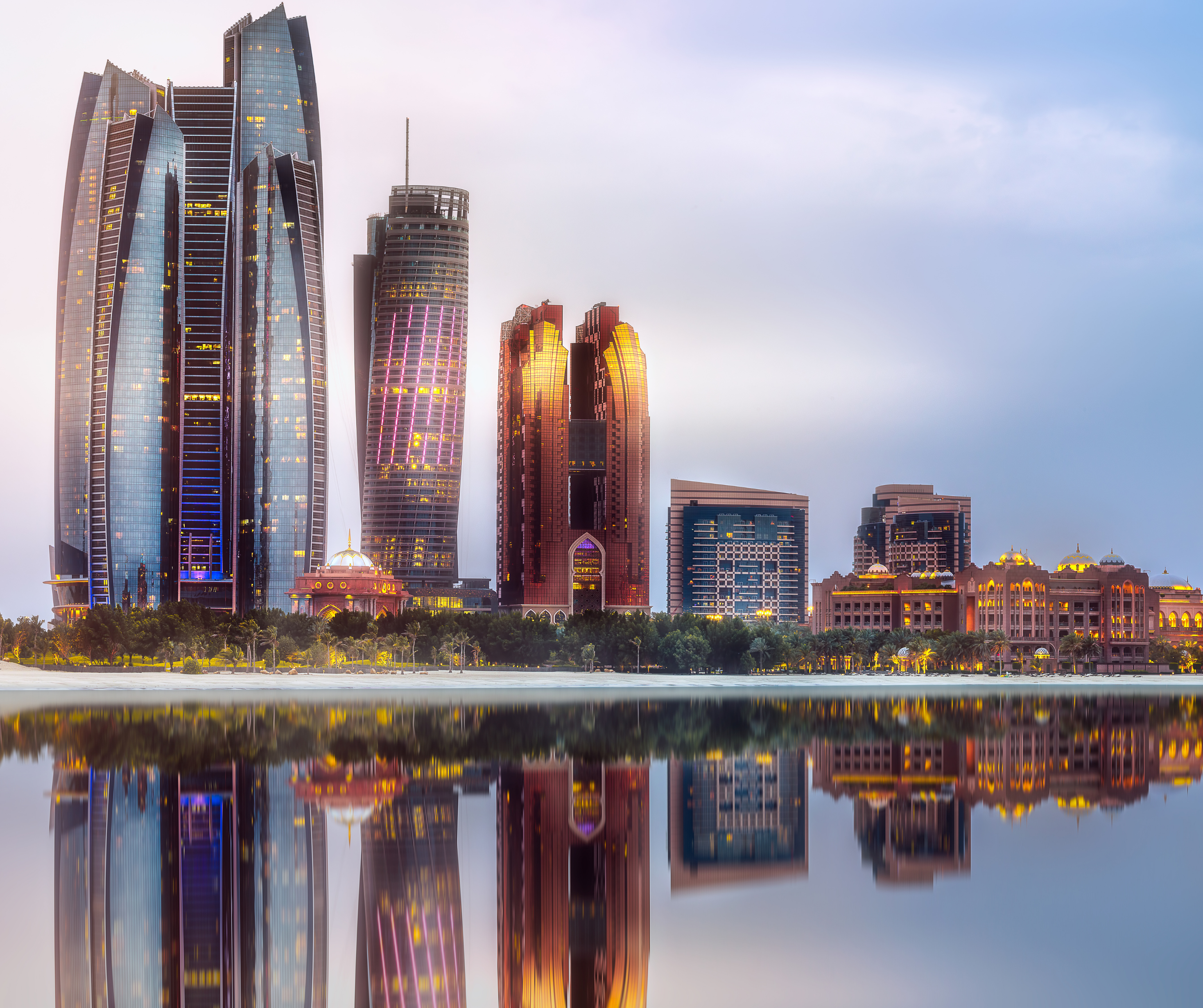 Twilight view of Abu Dhabi's Etihad Towers reflecting on calm waters.