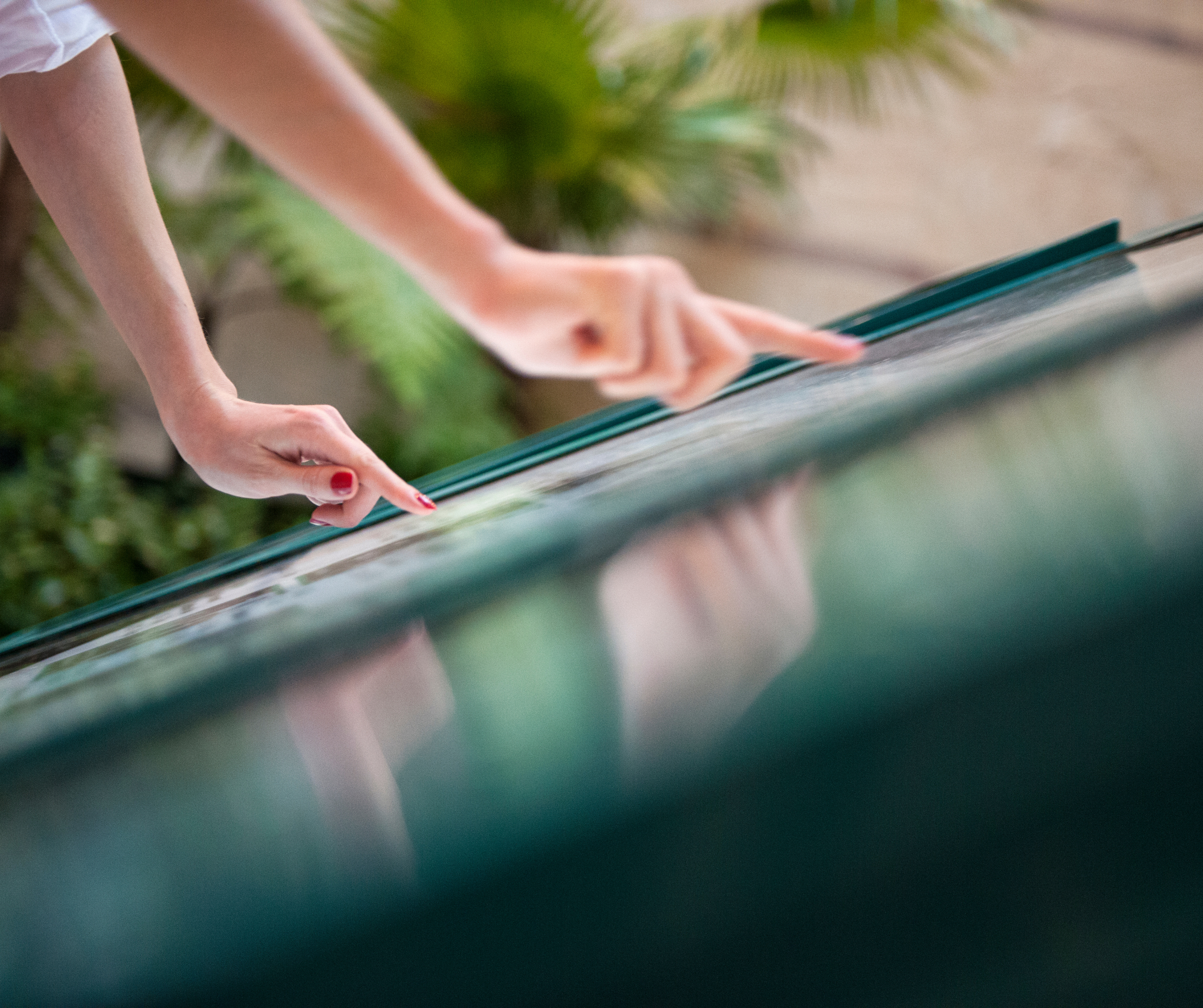 A close-up of a person's hands using a touchscreen display, with greenery in the background.