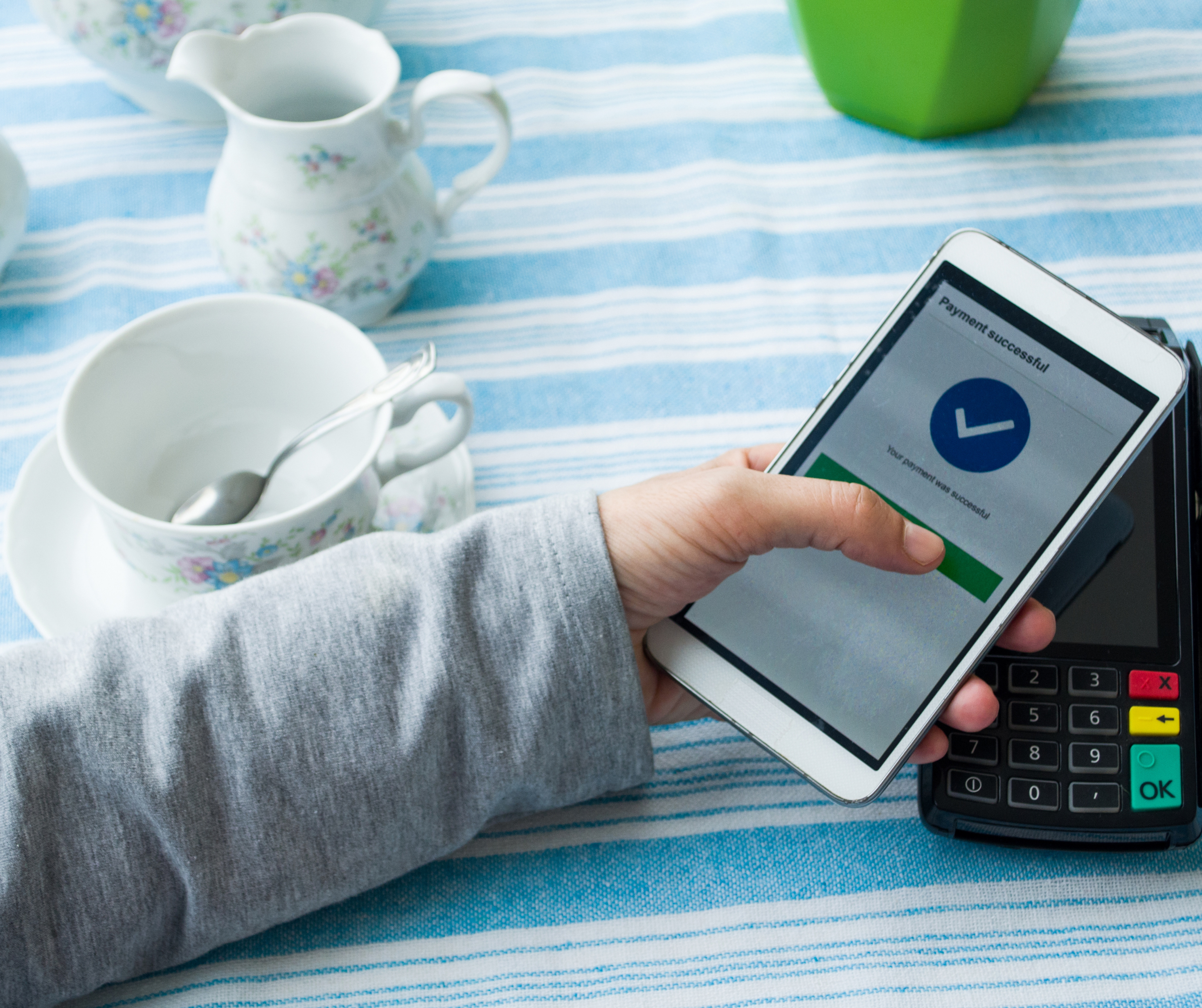 A person holding a smartphone displaying a "Payment successful" message near a contactless payment terminal.