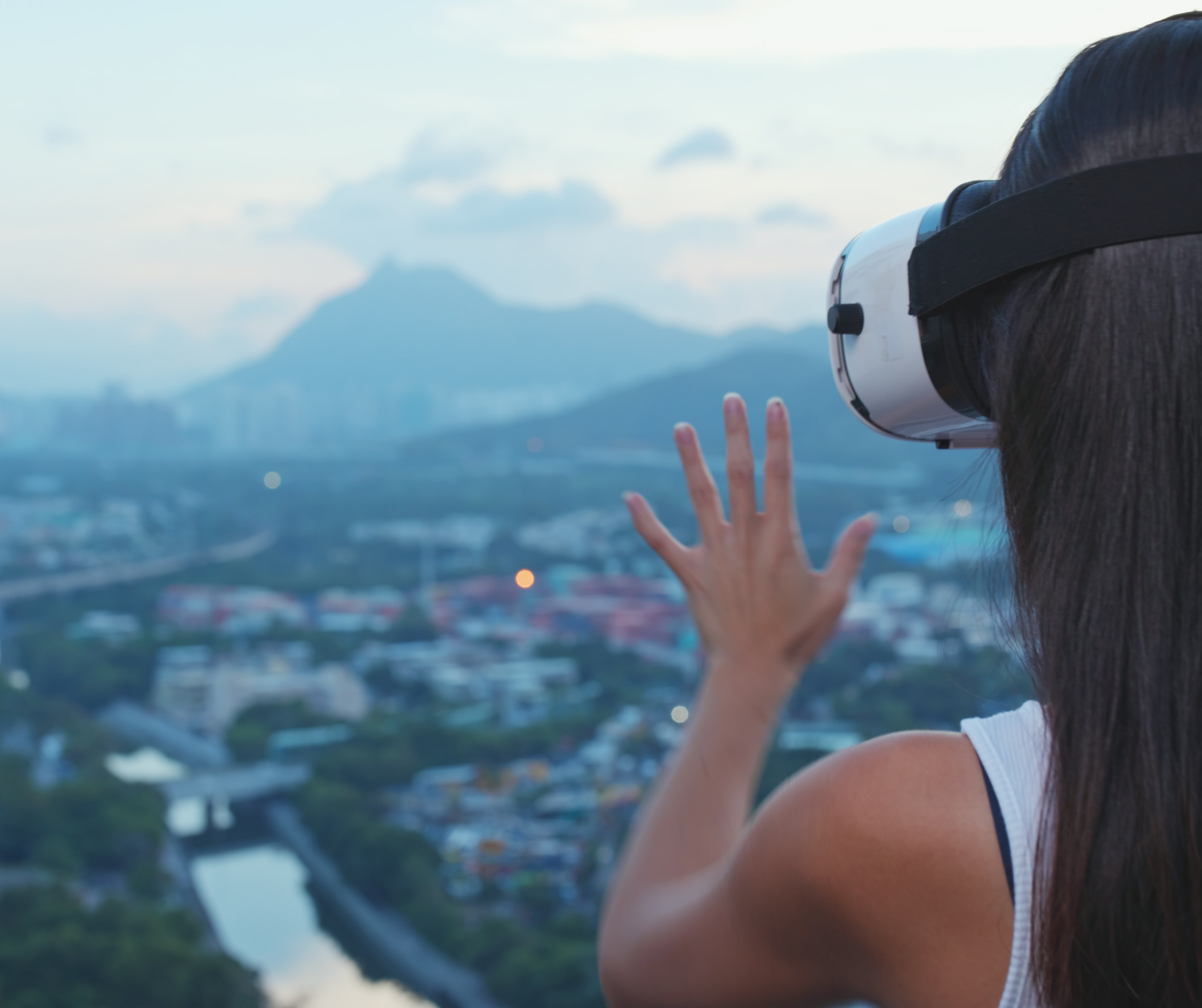 A person wearing a virtual reality headset and interacting with a virtual environment while overlooking a cityscape with mountains in the background.