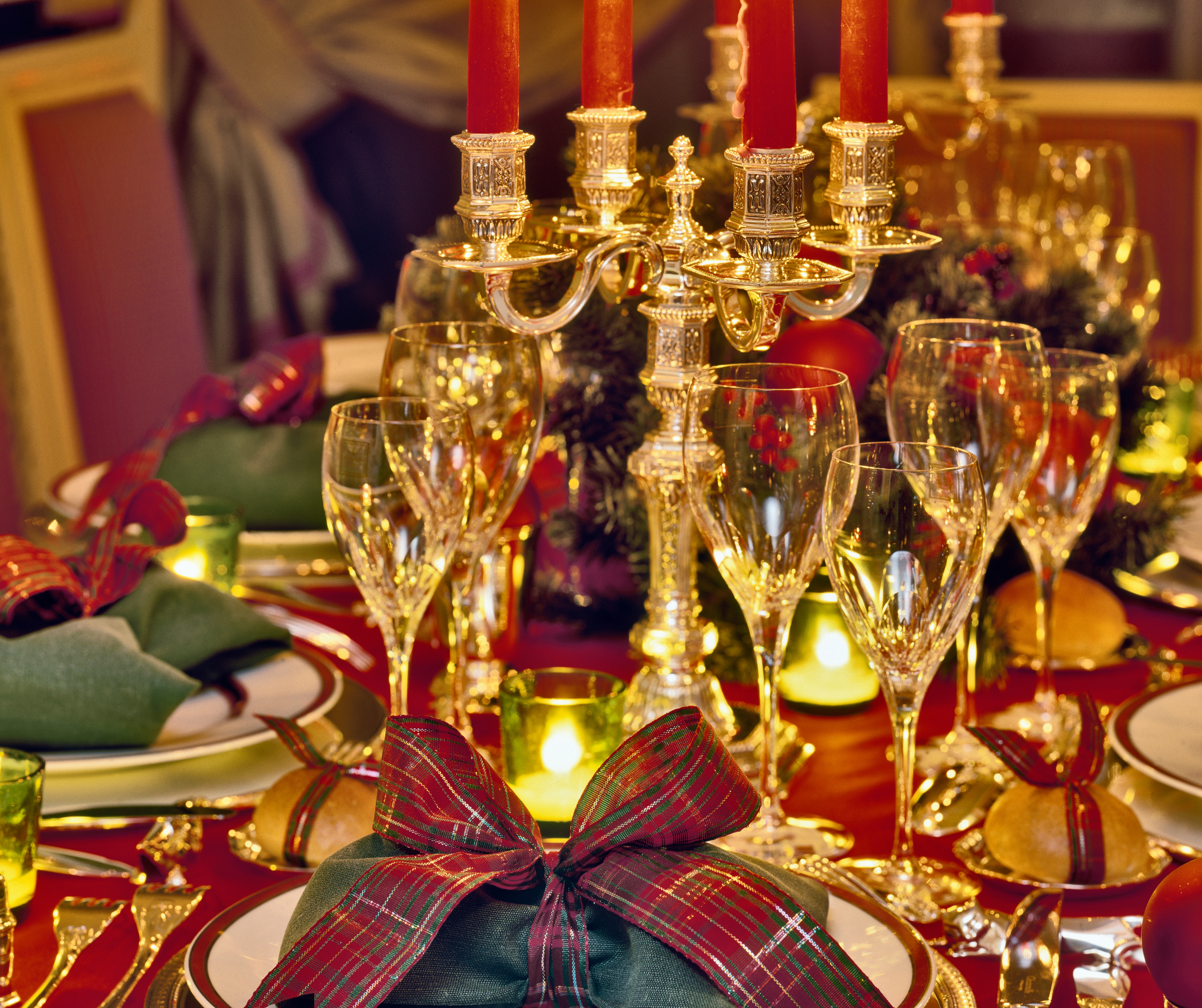 An elegantly set holiday dining table with red candles, crystal glassware, and festive red and green bows.