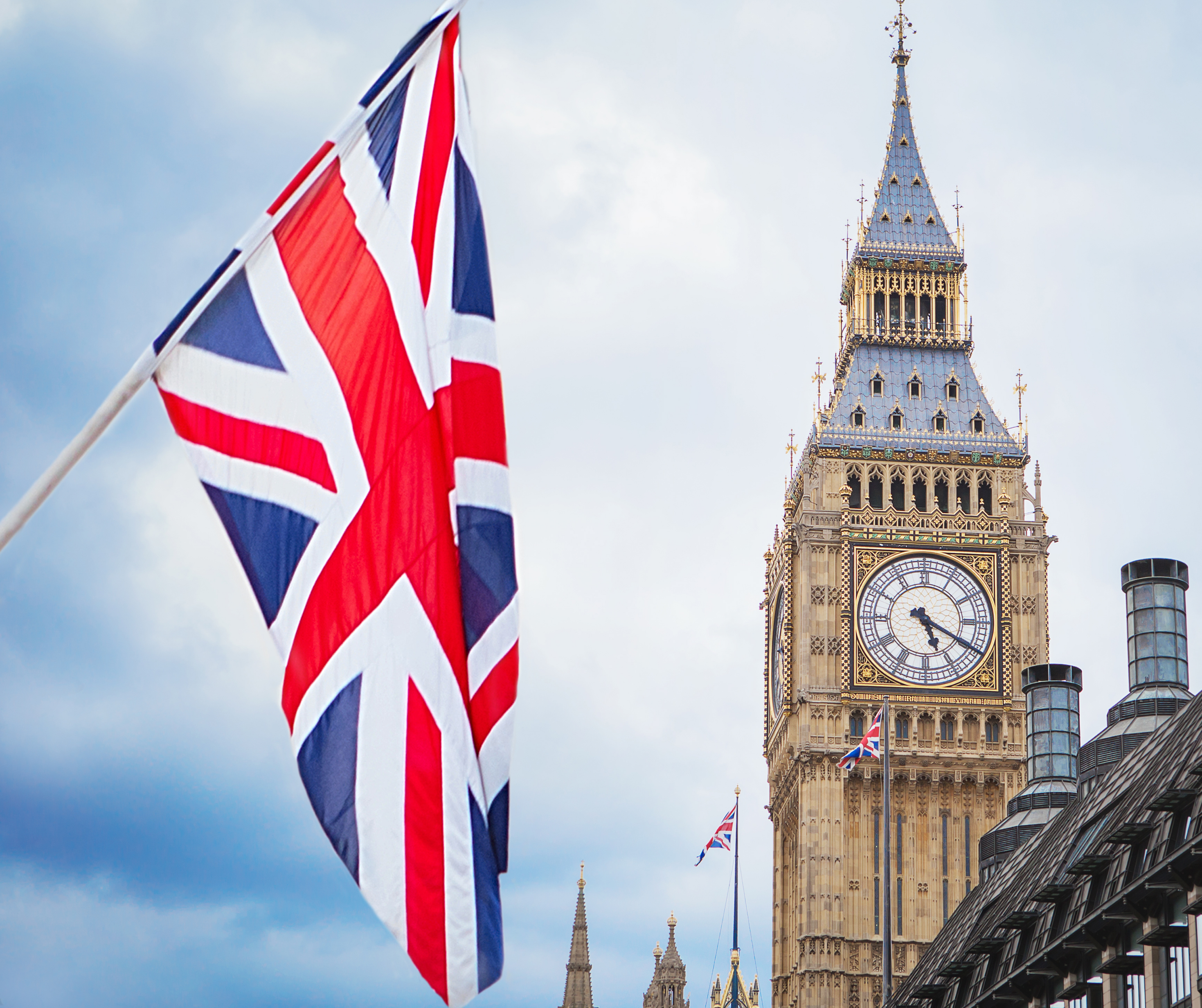 Union Jack flag flying in front of Big Ben clock tower in London on a cloudy day.