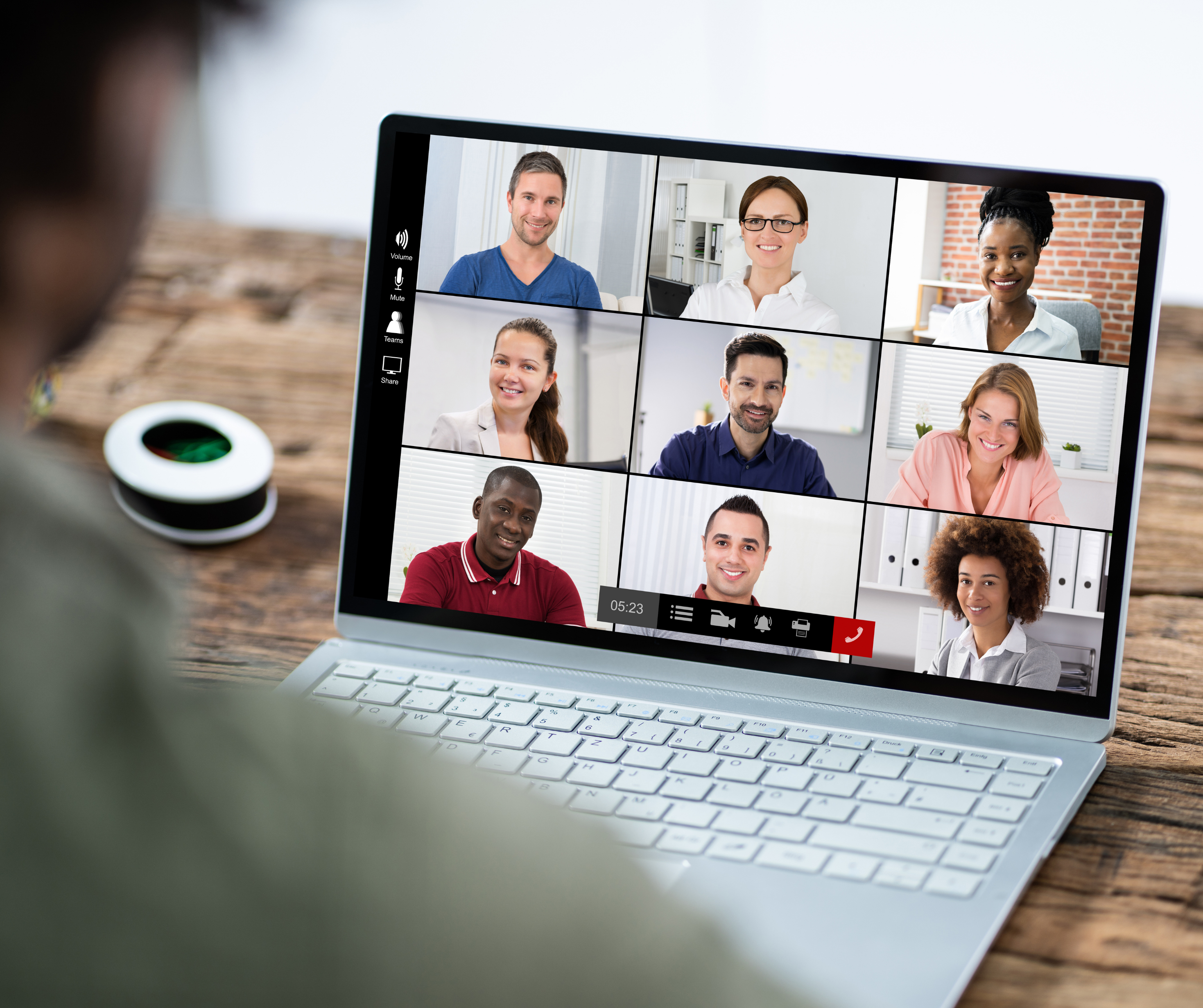 A person participating in a virtual meeting with eight other people displayed on a laptop screen.