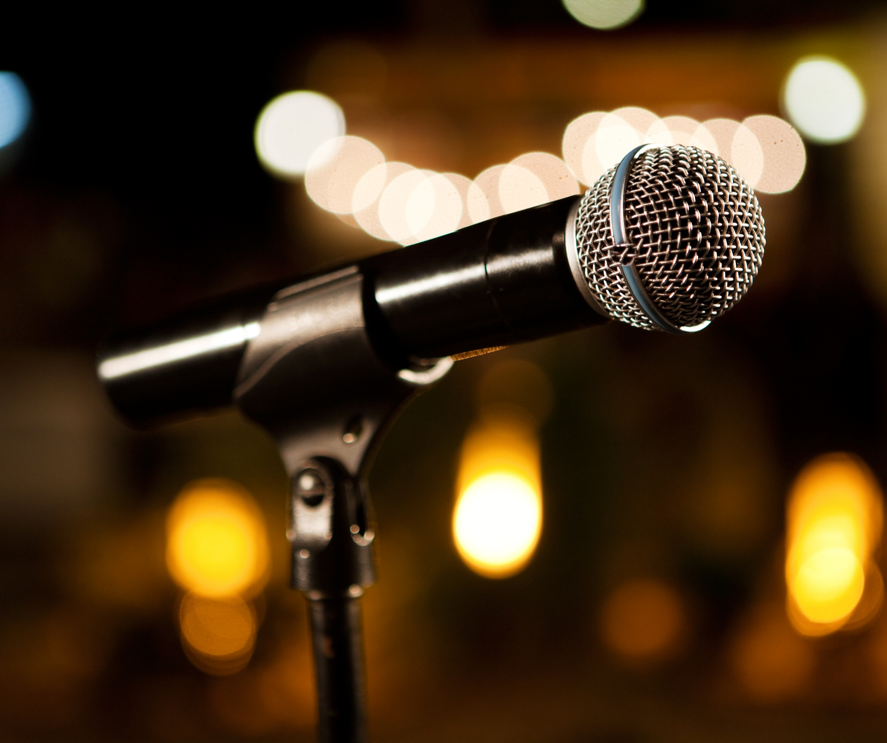 Close-up of a microphone on a stand with a blurred background featuring lights.