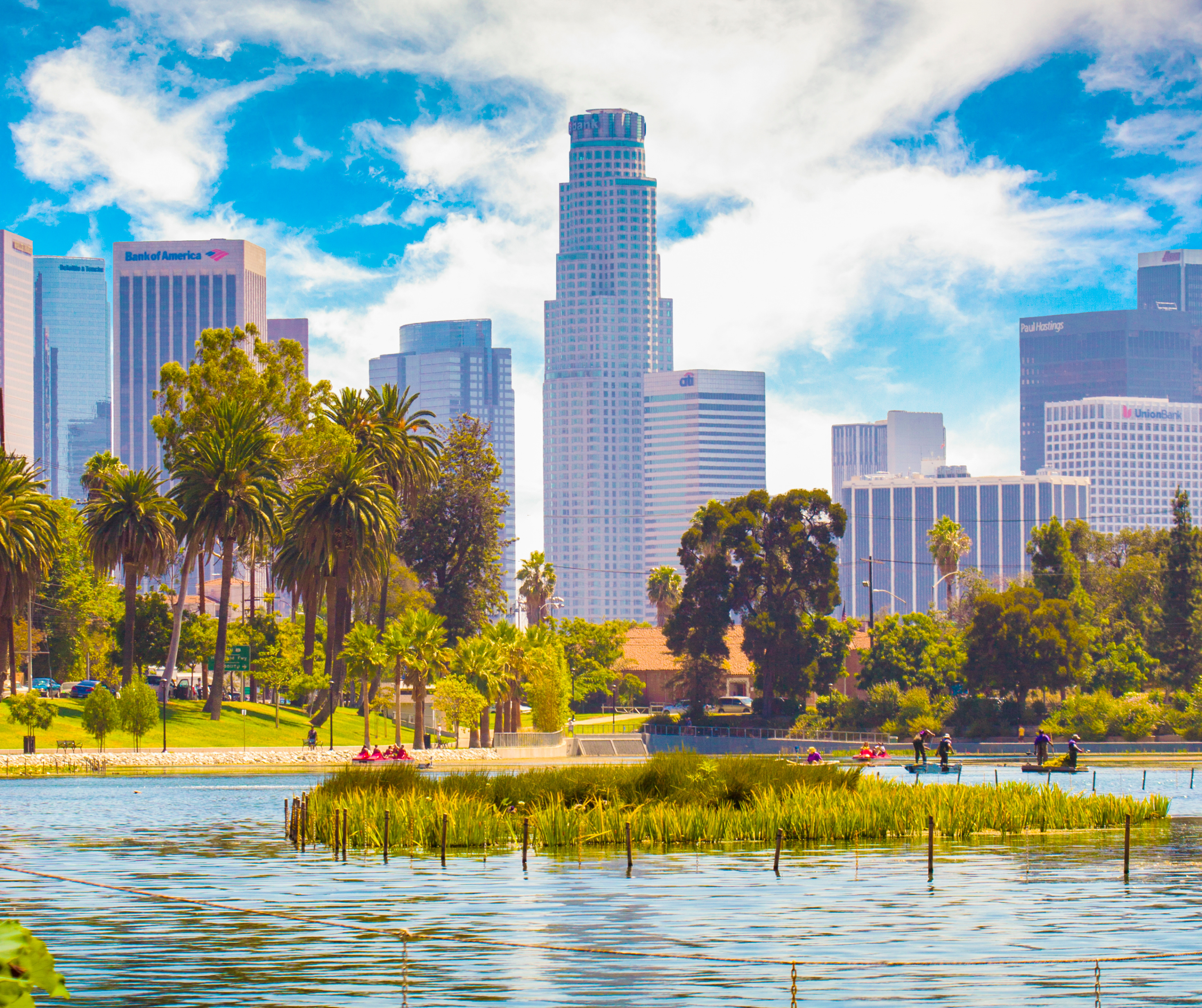 Panoramic view of Los Angeles downtown skyline with high-rises and palm trees viewed from across a lake in Echo Park.