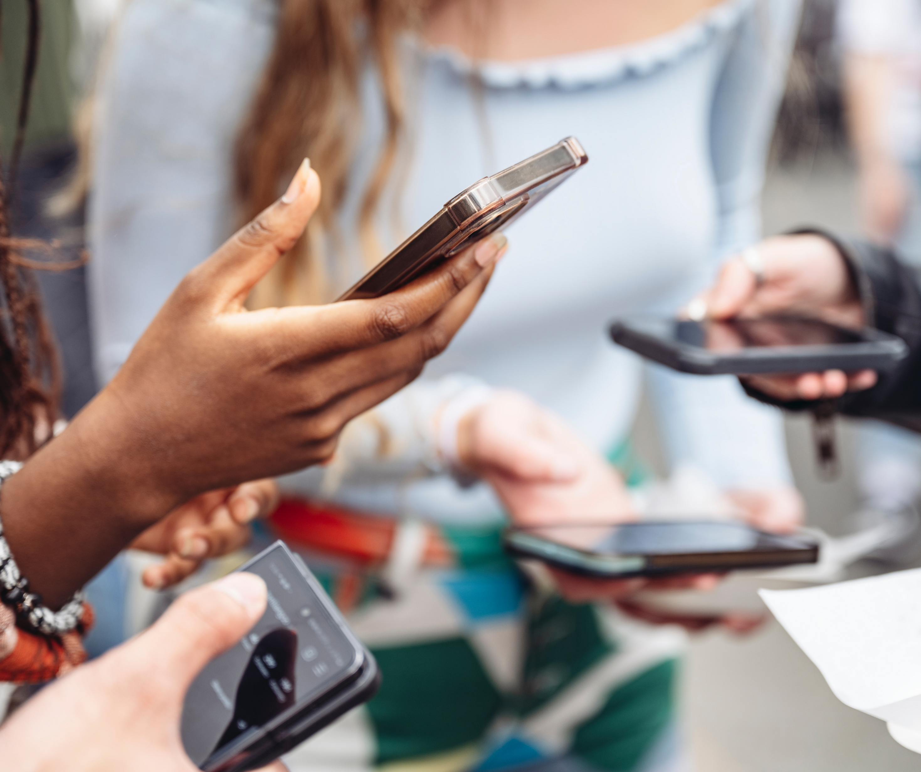 Group of people holding and using smartphones, with a focus on their hands and devices.