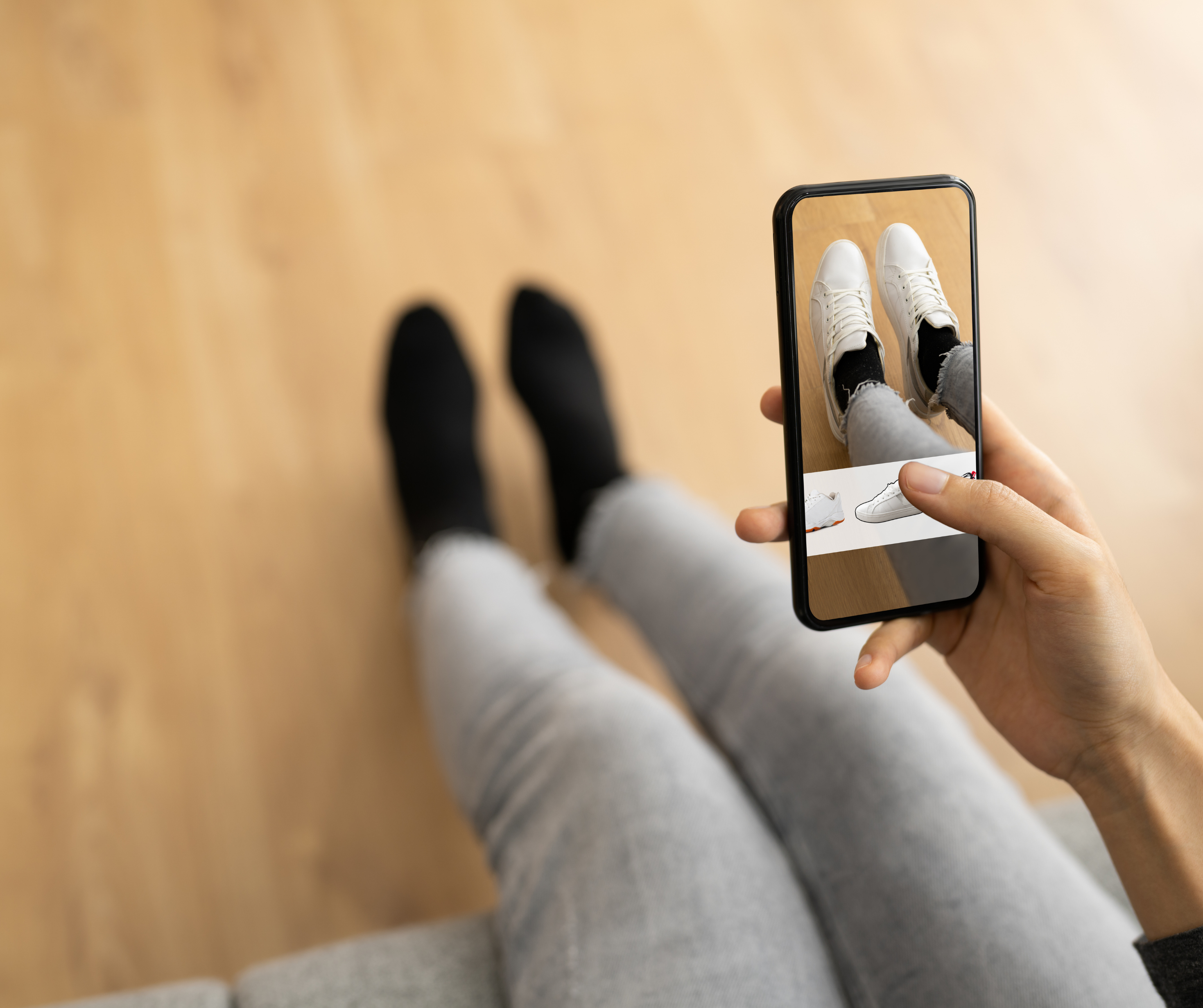 Person using a smartphone to virtually try on white sneakers while wearing black socks.