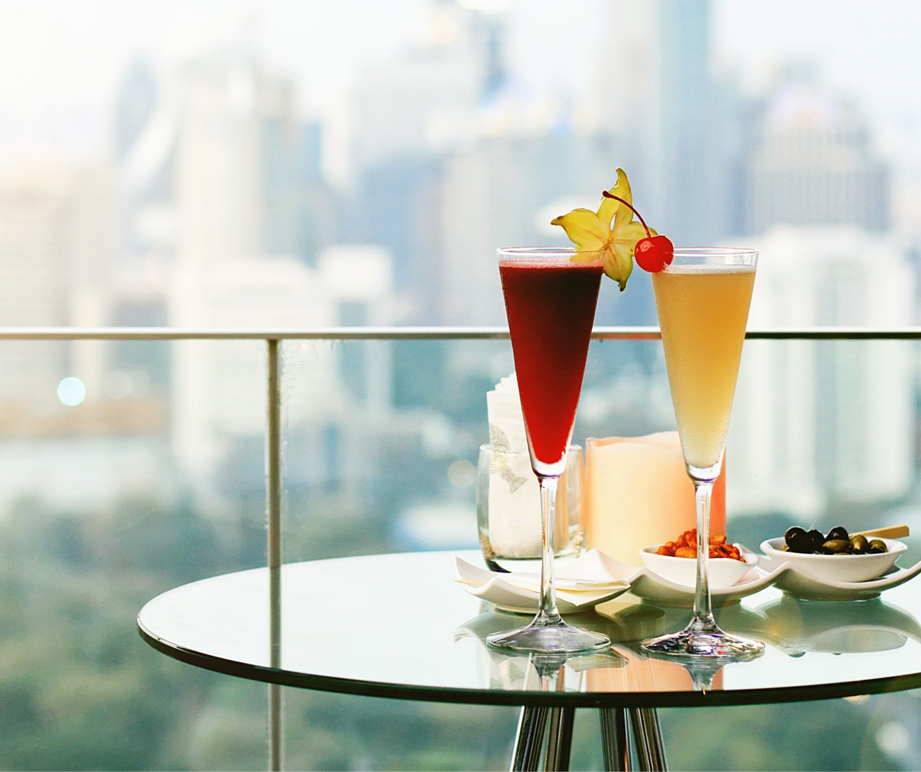 Two cocktails on a rooftop bar with a cityscape in the background.