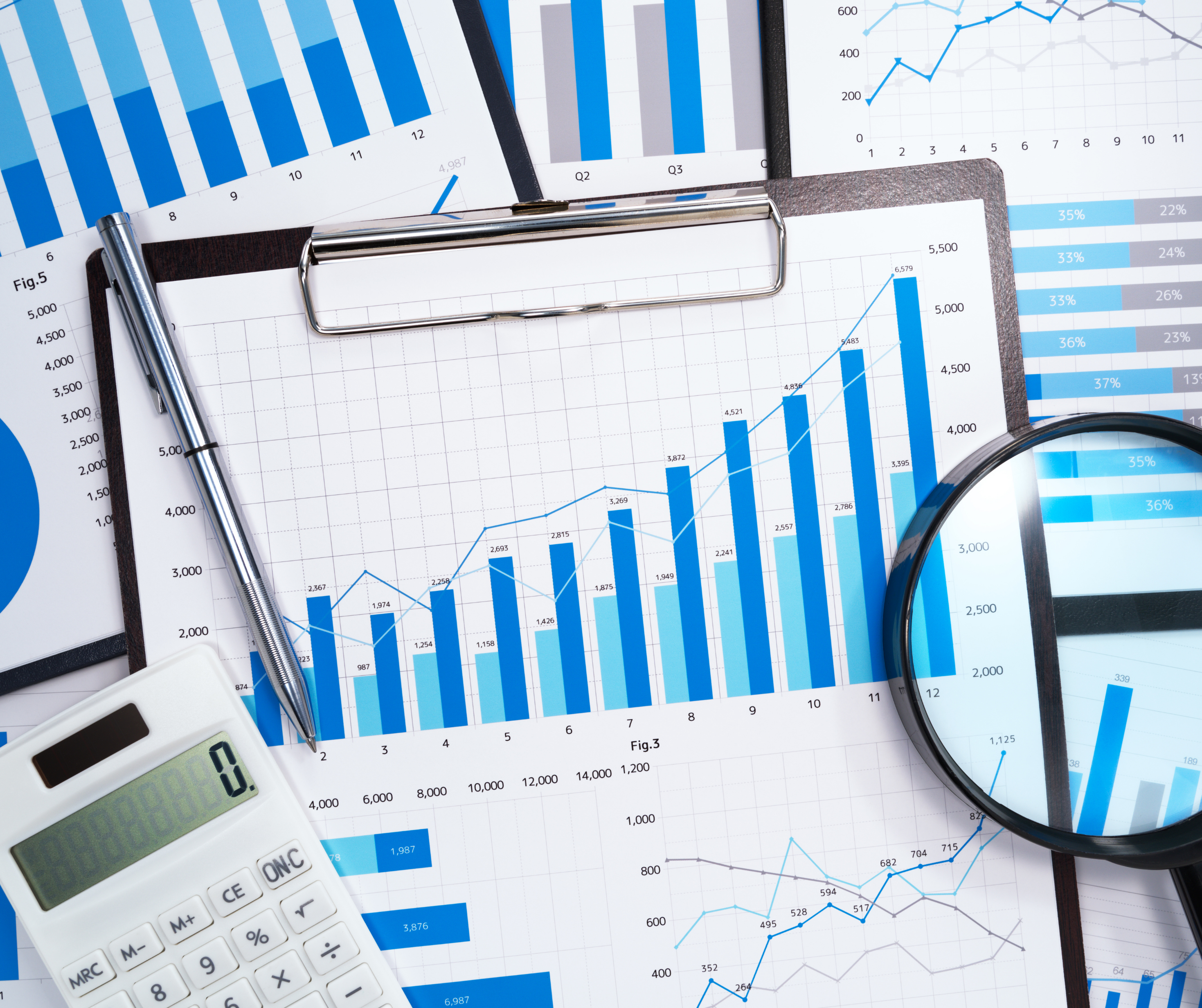 A collection of business charts and graphs spread out on a table, accompanied by a magnifying glass, pen, and calculator.