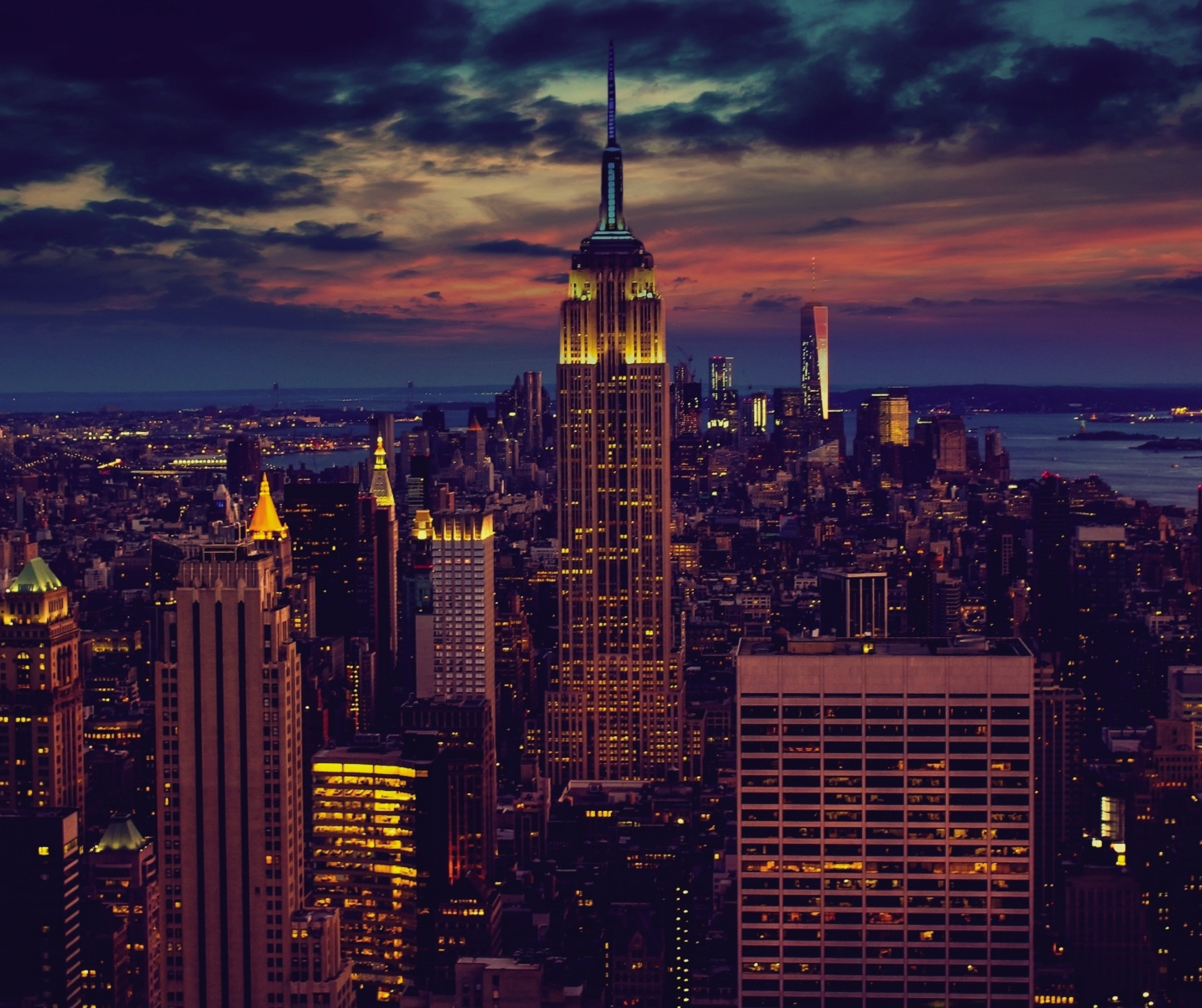 New York City skyline at dusk with iconic skyscrapers, city lights reflecting off the Hudson River, and Central Park in the foreground.