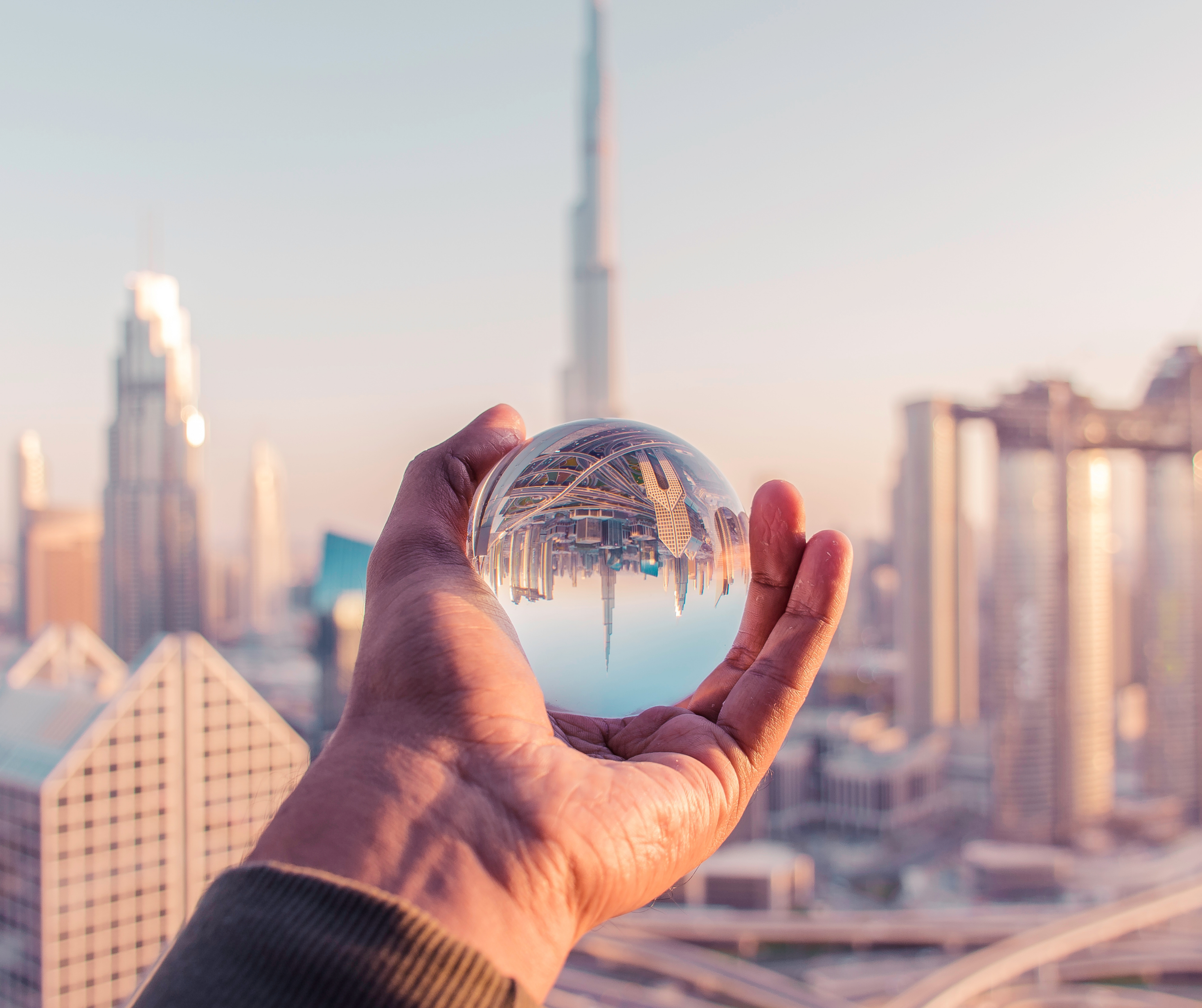 Hand holding a crystal ball reflecting an upside-down cityscape, with modern skyscrapers visible in the background.