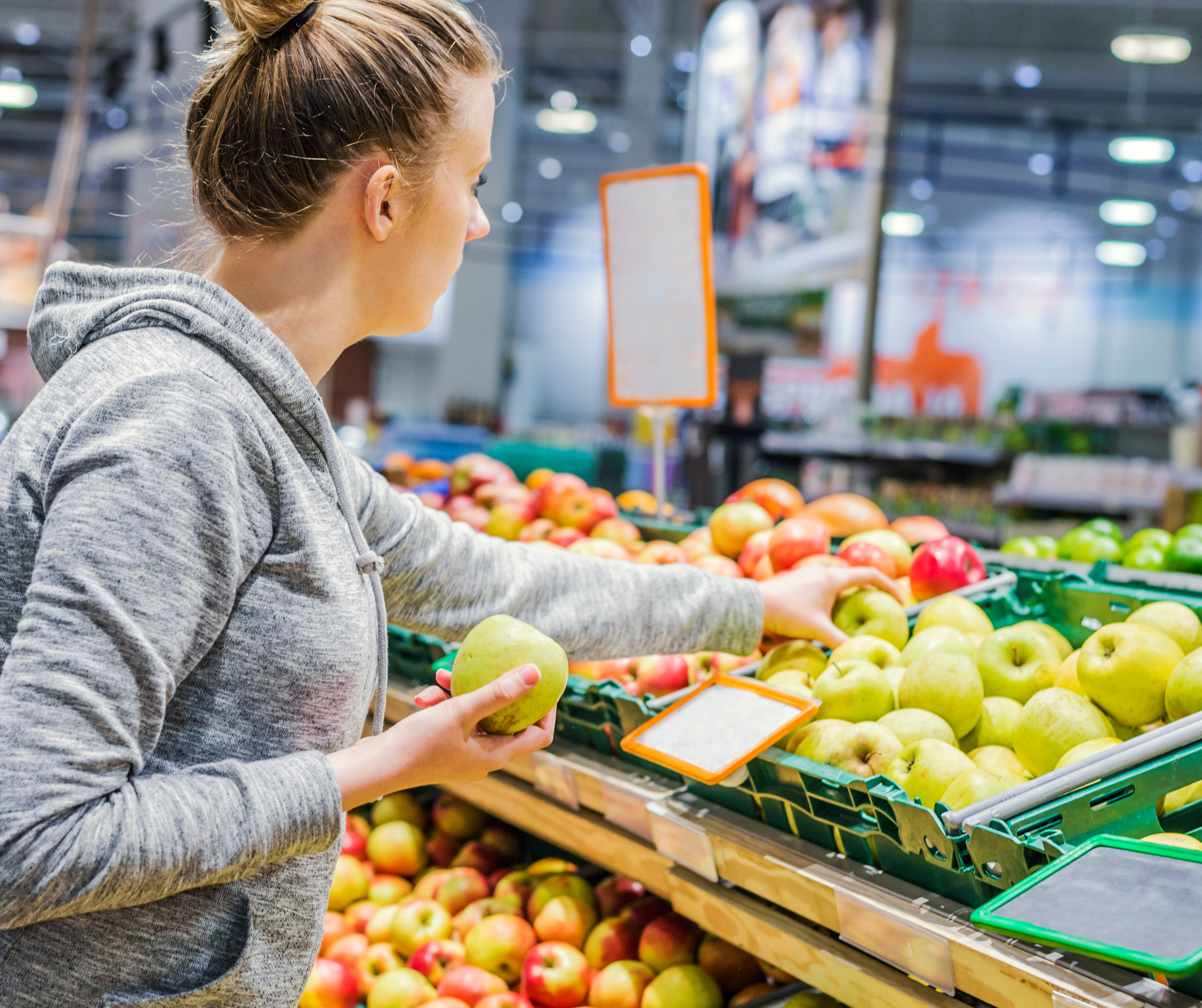 Woman choosing apples from a produce section in a grocery store