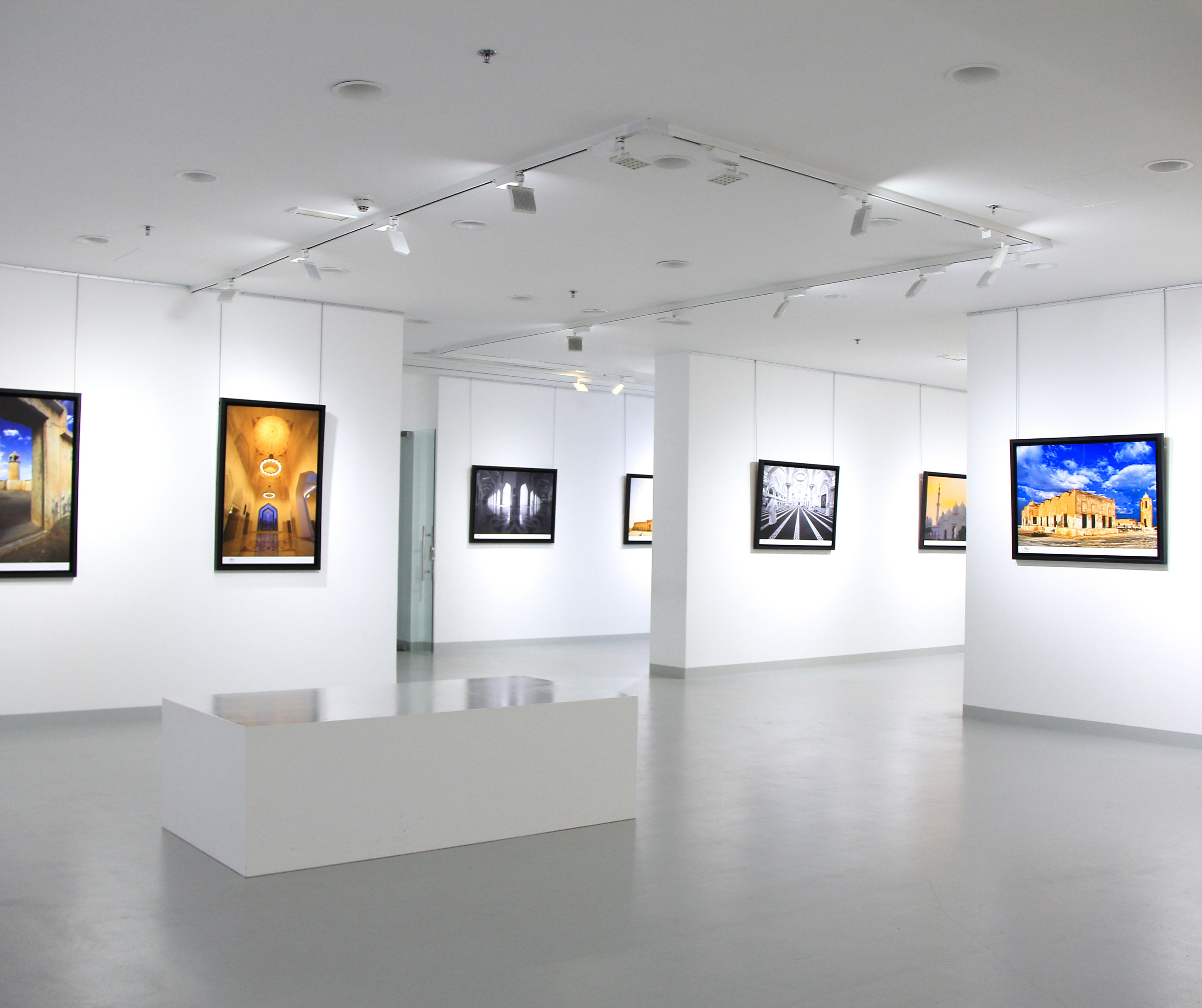 Interior view of a modern art gallery with white walls, track lighting, and various framed artworks on display.