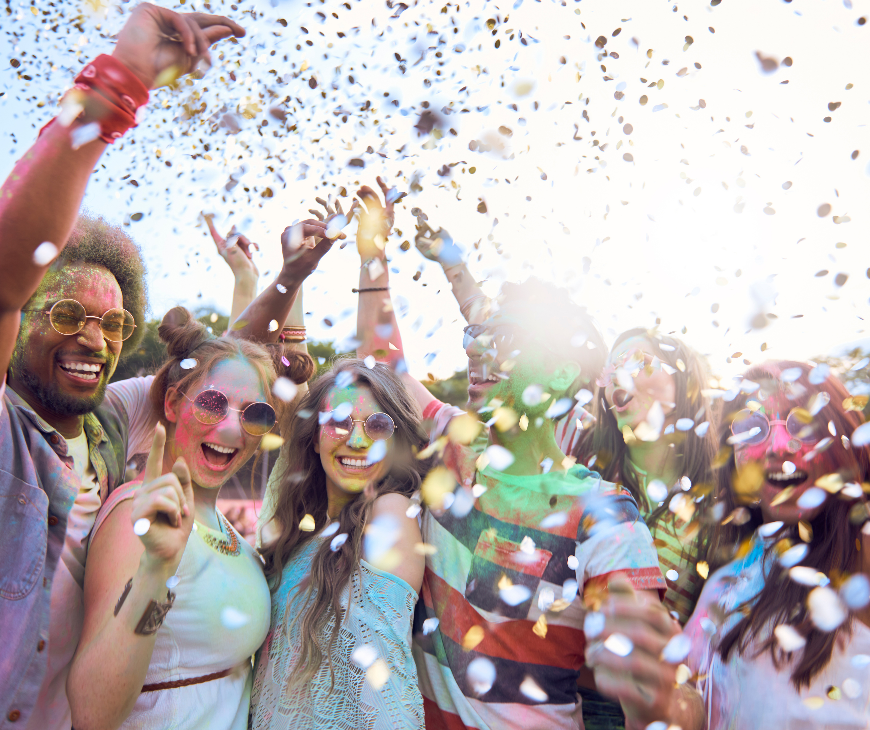 A group of friends joyfully celebrating with colorful confetti in the air at an outdoor festival.