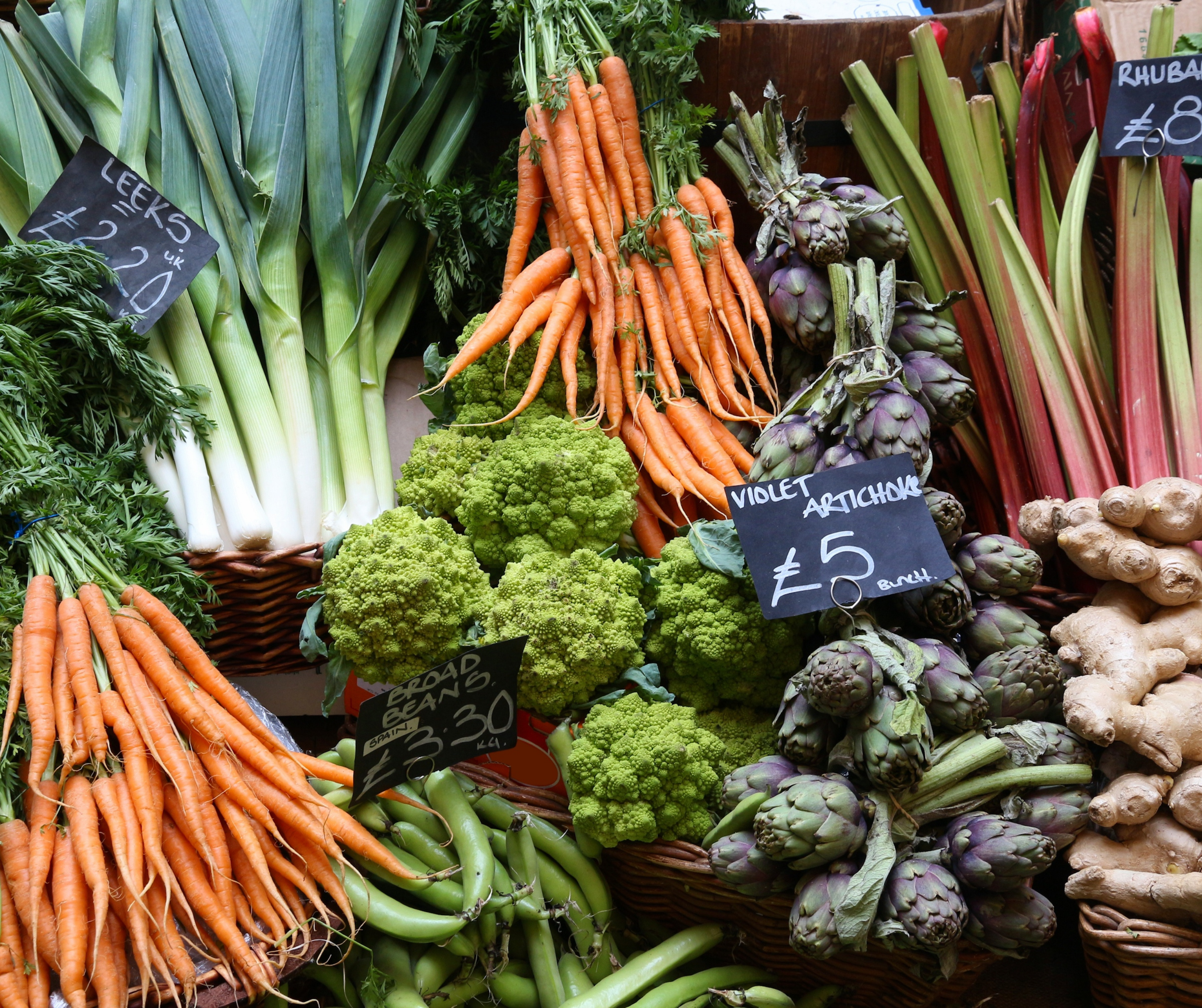 Assorted fresh vegetables including leeks, carrots, artichokes, and rhubarb at a farmer's market.