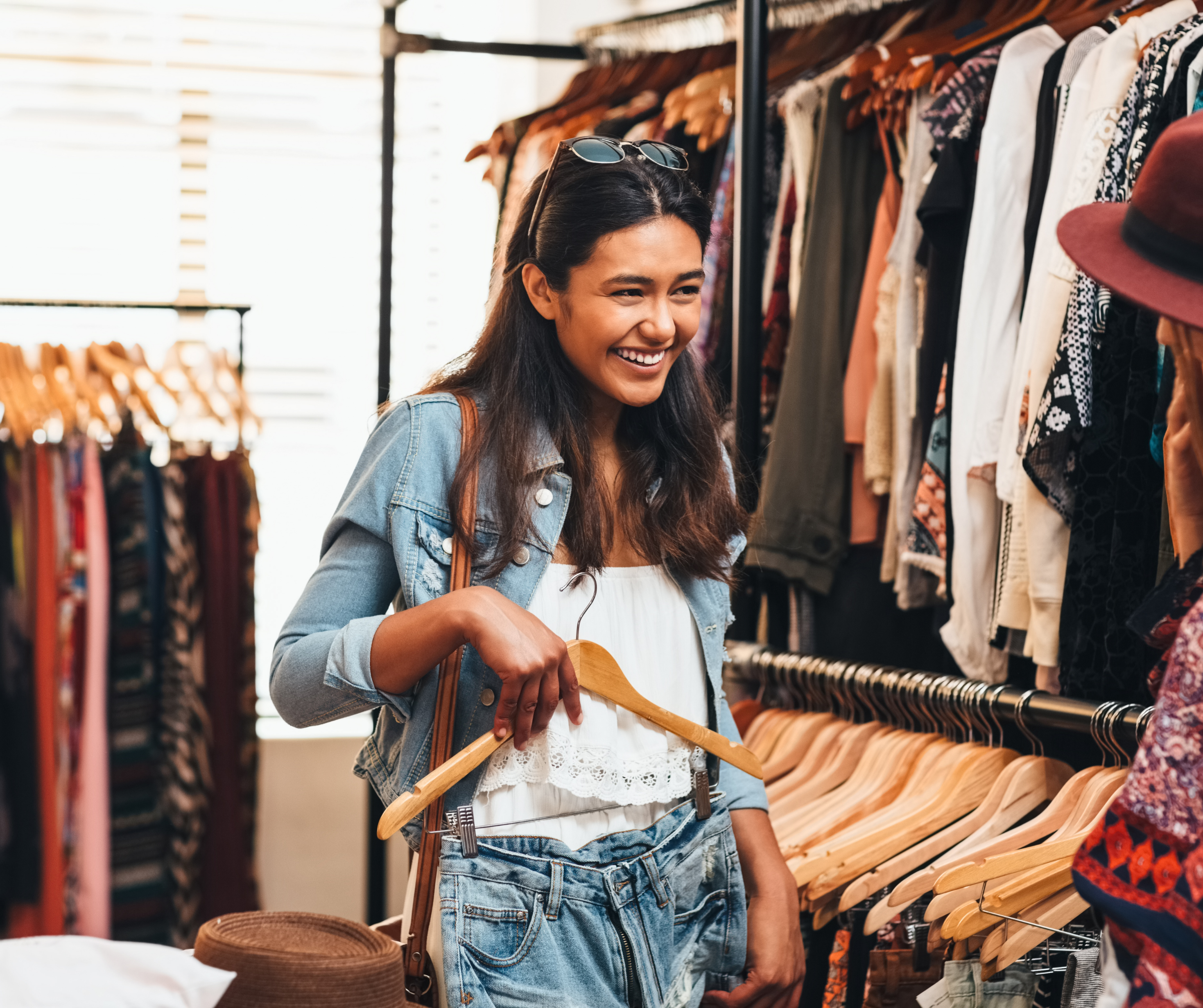 A smiling woman holding a hanger while shopping for clothes in a boutique.