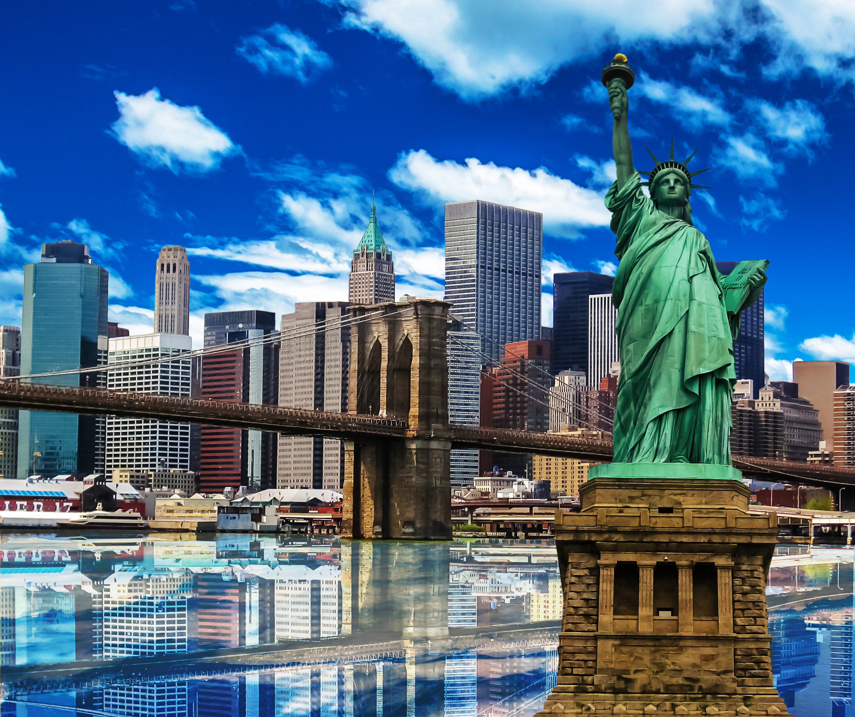 Statue of Liberty with the Brooklyn Bridge and New York City skyscrapers under a bright blue sky with clouds.