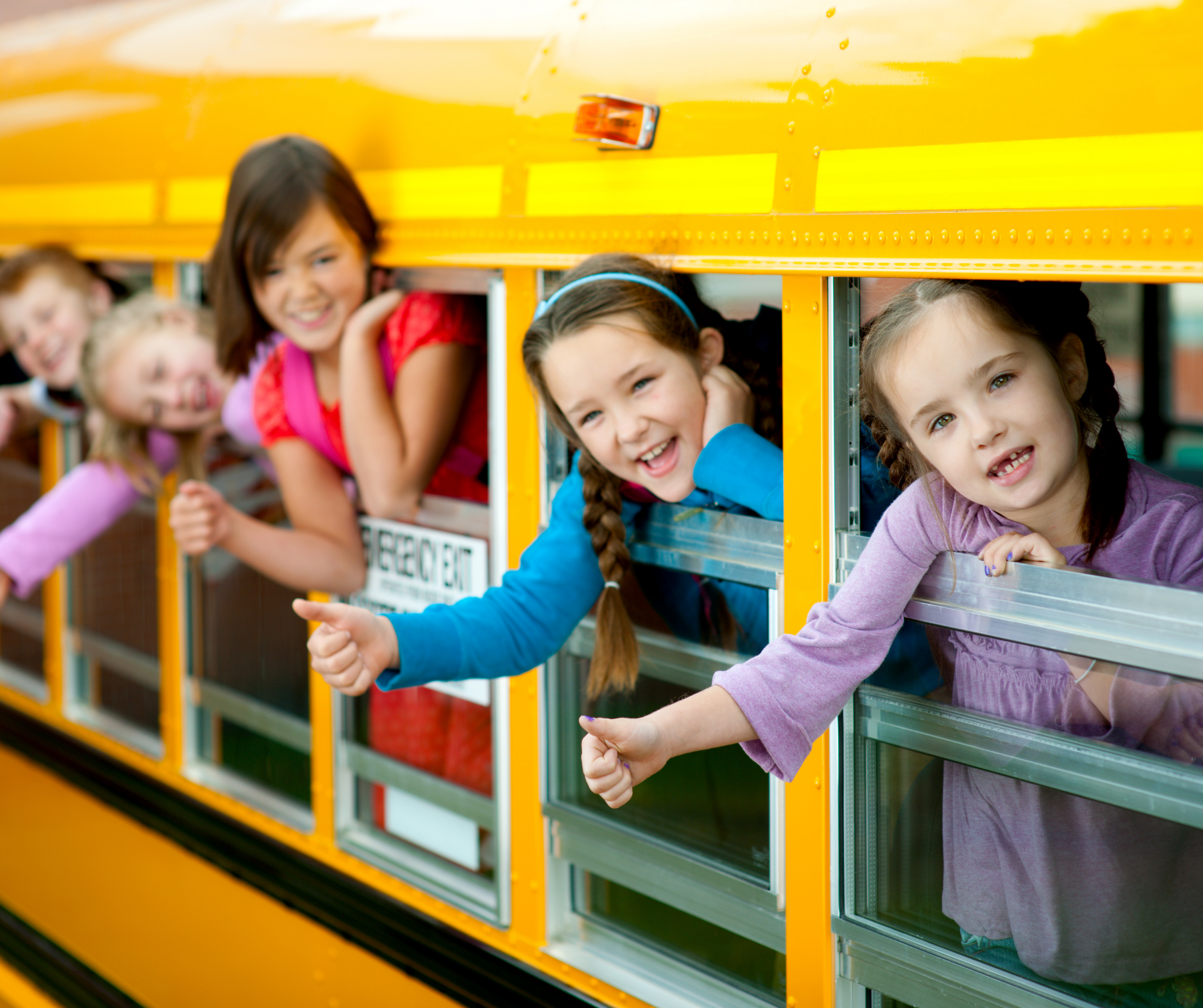 A group of cheerful school kids sitting in a school bus, smiling and waving from the windows