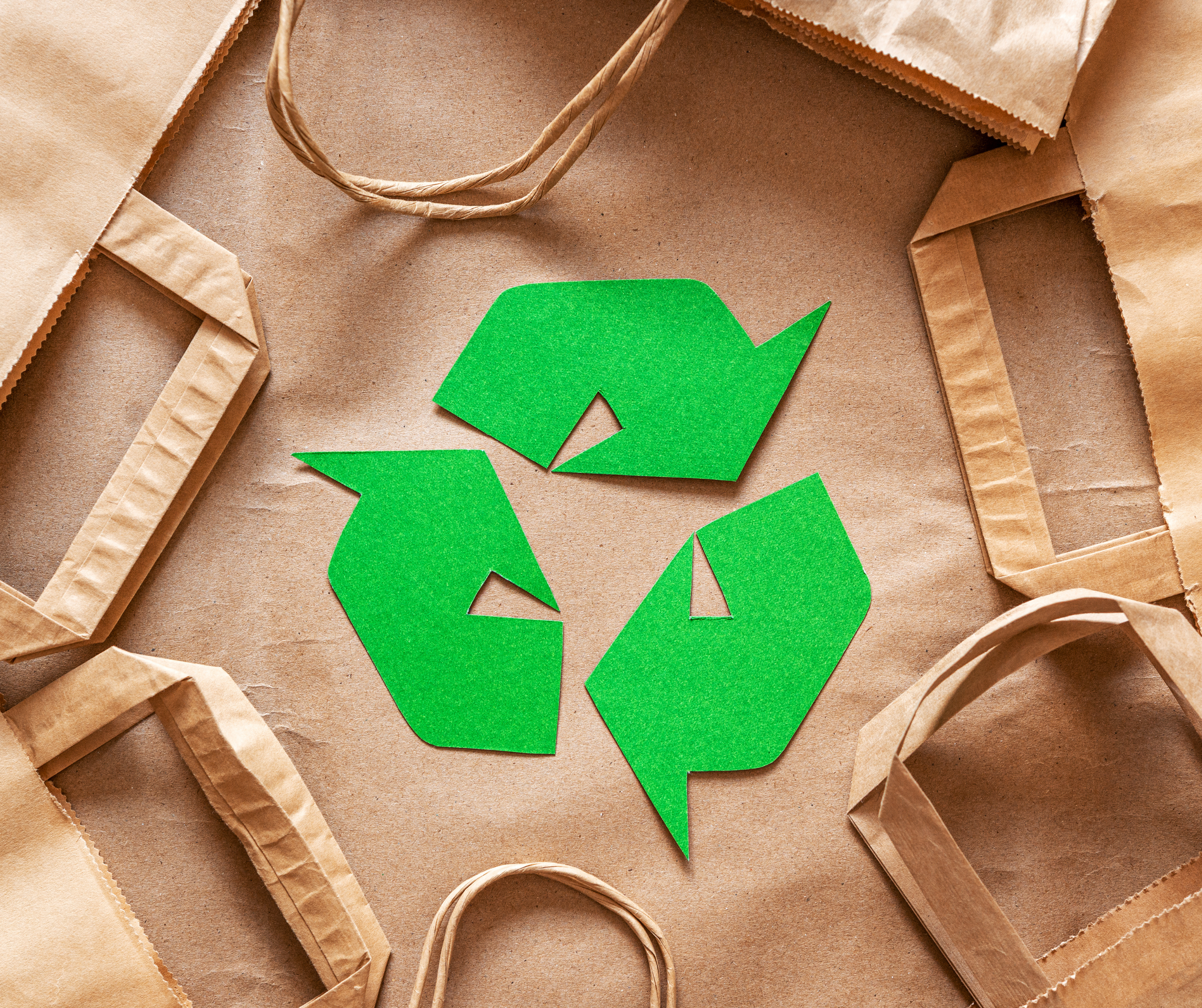 Green recycling symbol surrounded by brown paper bags on a brown background."