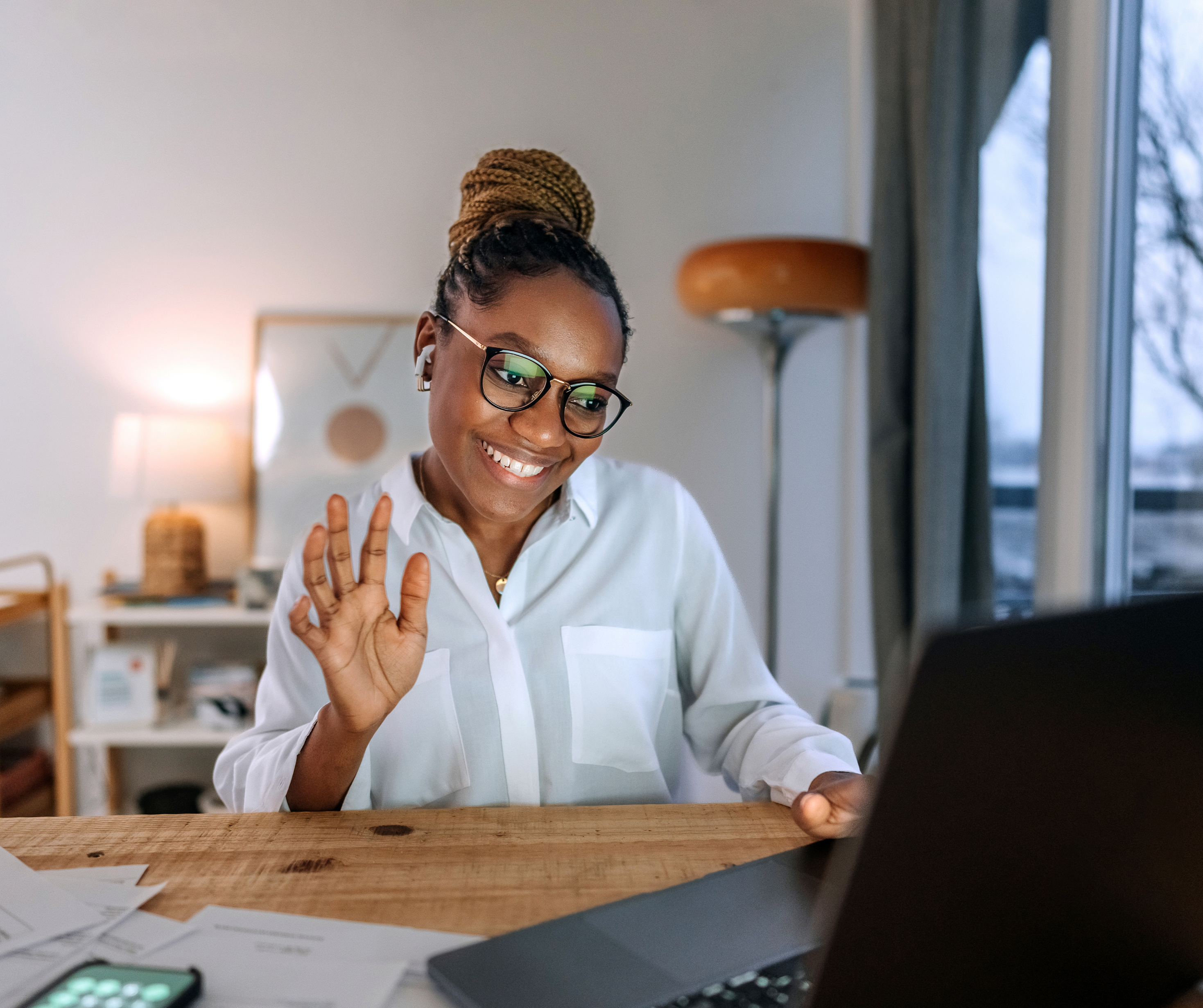 Person smiling and waving at a laptop screen during a virtual meeting.