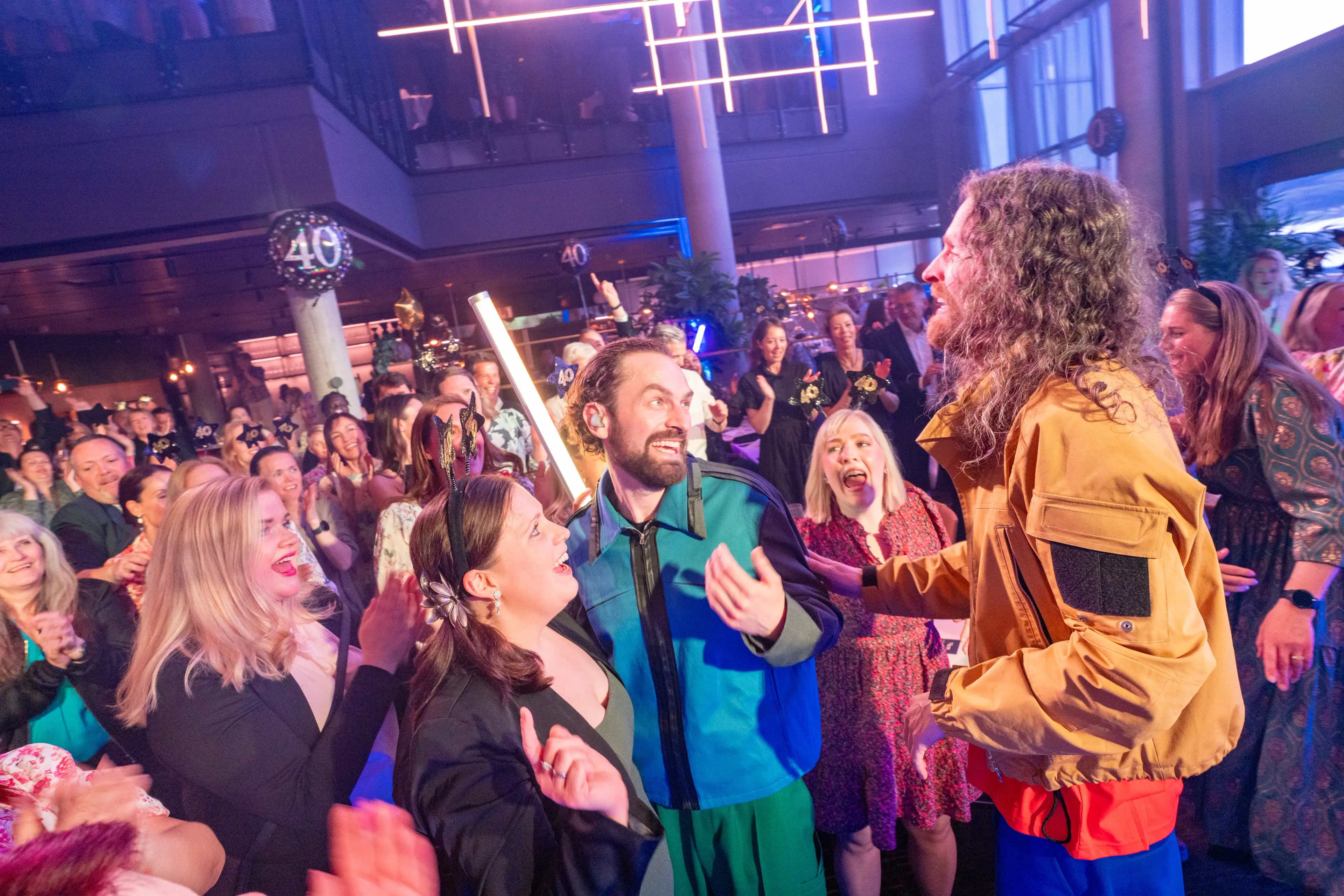 Medlemmene i Sirkus Eliassen står midt blant et entusiastisk publikum under jubileumsfesten på Quality Hotel Richard With. Deltakerne smiler, klapper og tar bilder.