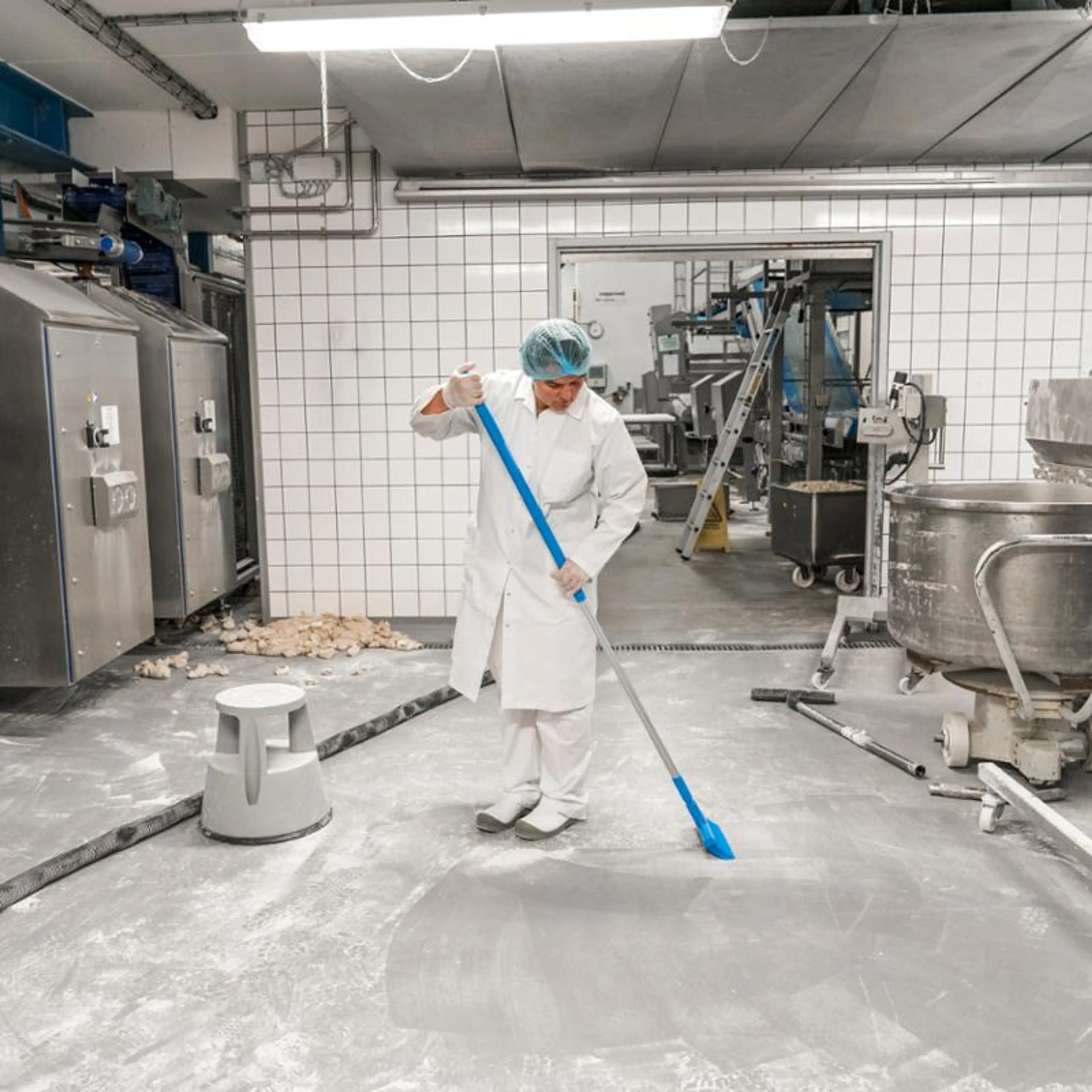Person i hvit frakk som vasker gulvet i et produksjonslokalet