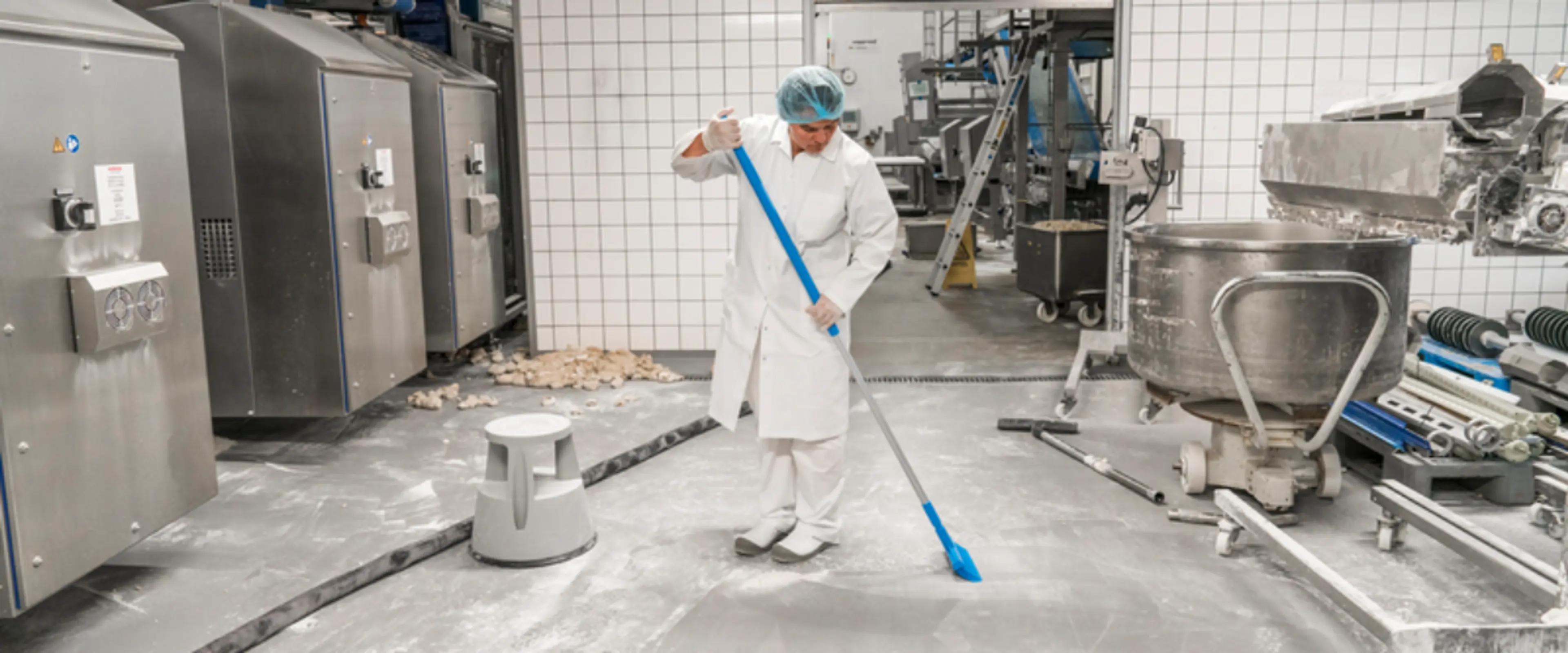 Person i hvit frakk som vasker gulvet i et produksjonslokalet