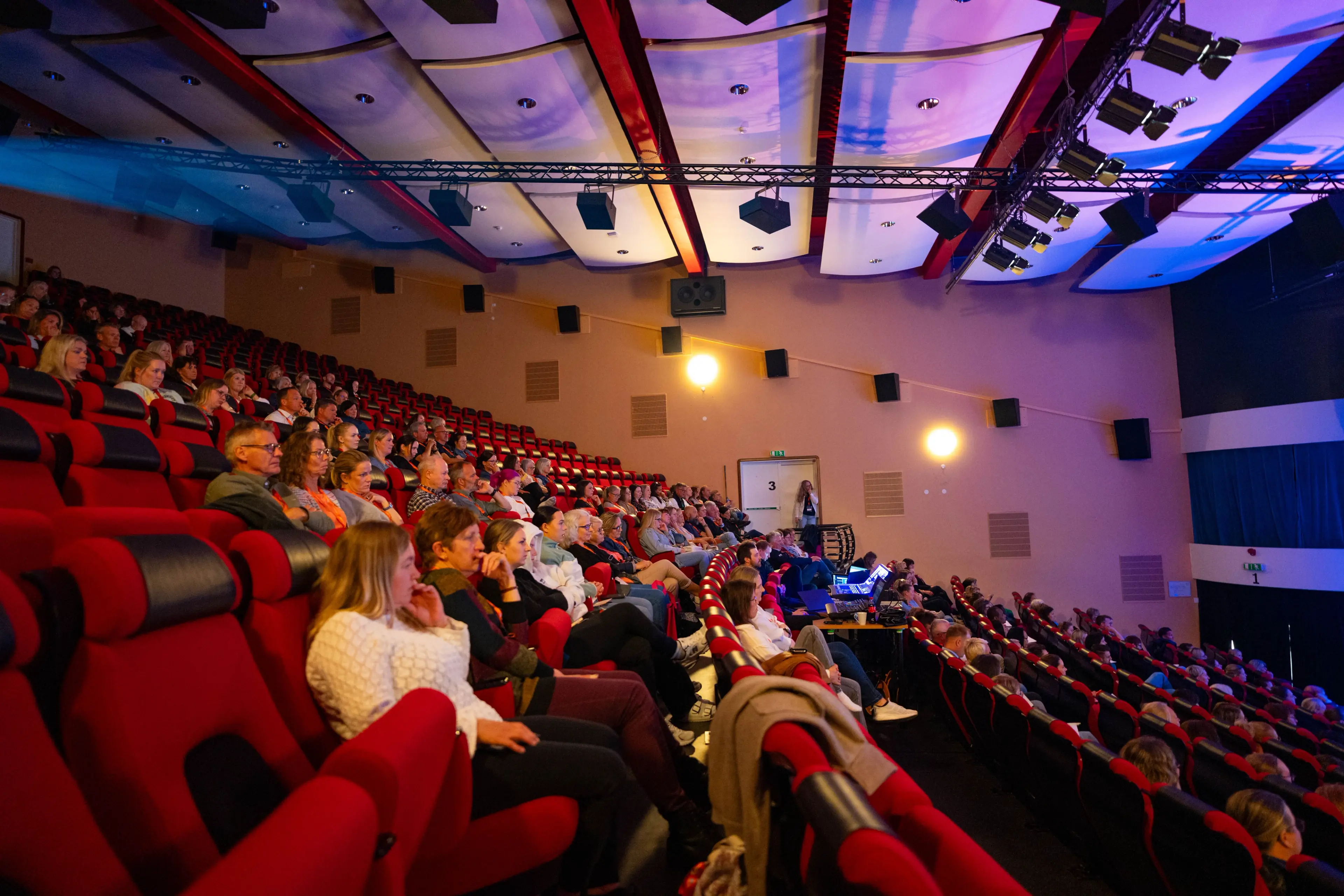 Deltakere sitter i røde stoler og følger engasjert med under et faglig foredrag under Helsedagene 2025.