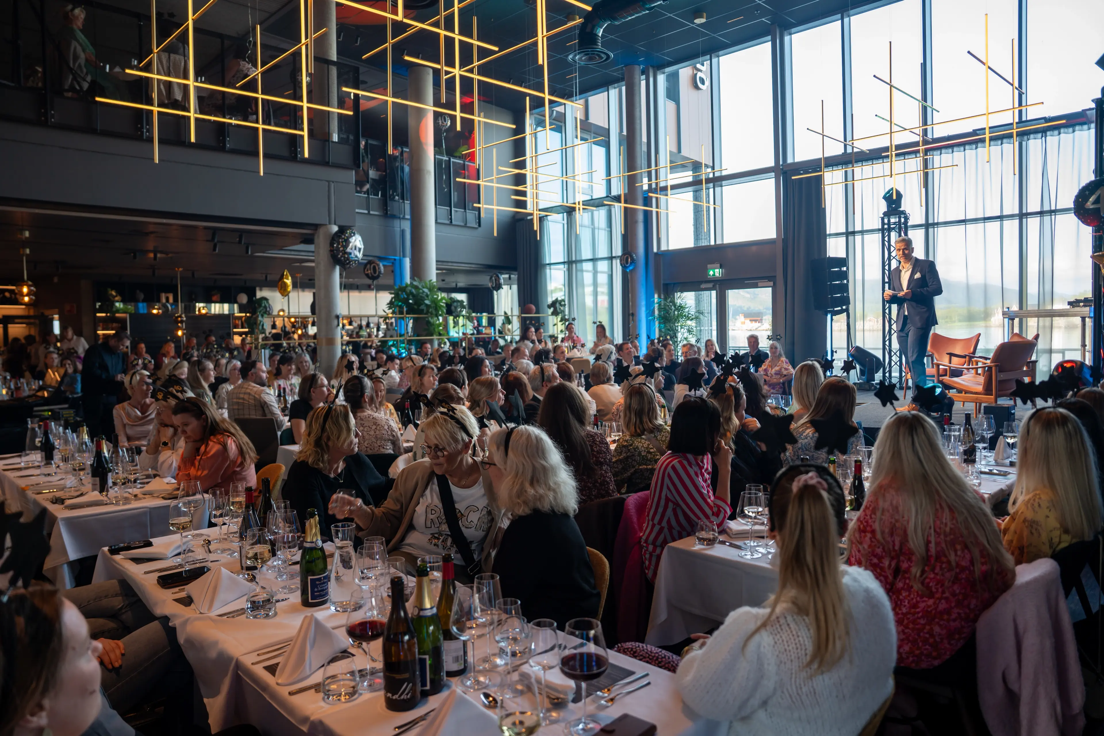 Festpyntede deltakere sitter til bords og lytter til konferansier Ronny Fyhn Hansen under jubileumsmiddagen på Quality Hotel Richard With under Helsedagene 2025.