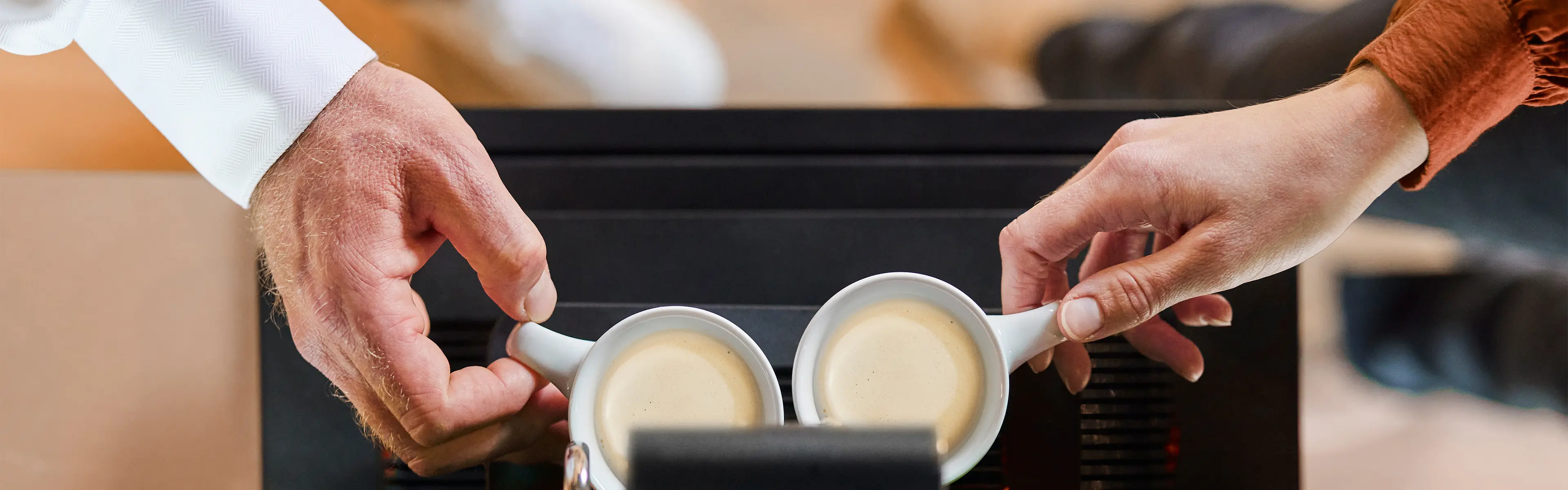 Bildet viser en mannehånd og en kvinnehånd som tar hver sin kopp nytraktet kaffe