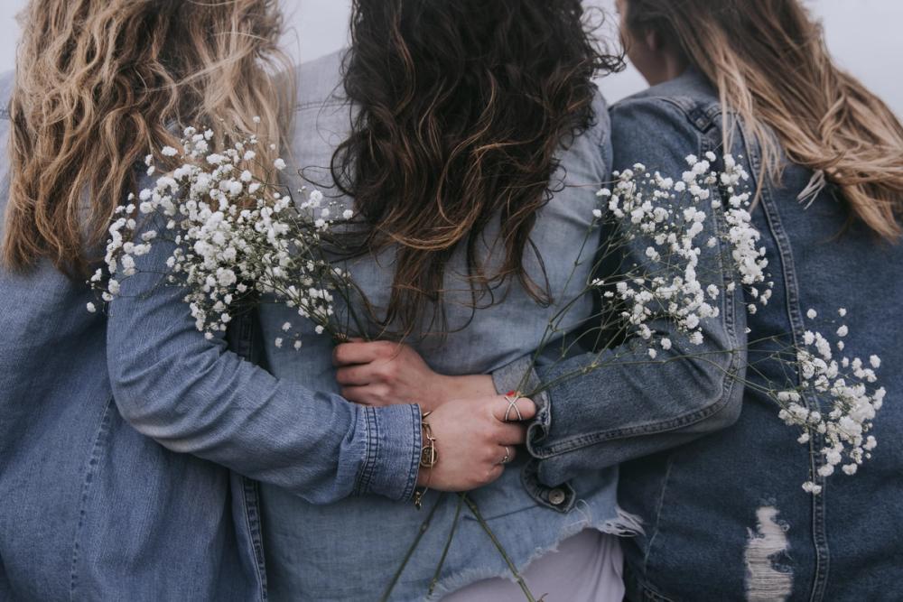 Tre kvinner som holder rundt hverandre med blomster i hendene