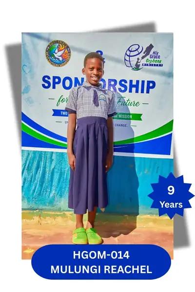 Girl in a navy plaid pinafore school dress and green sandals, smiling