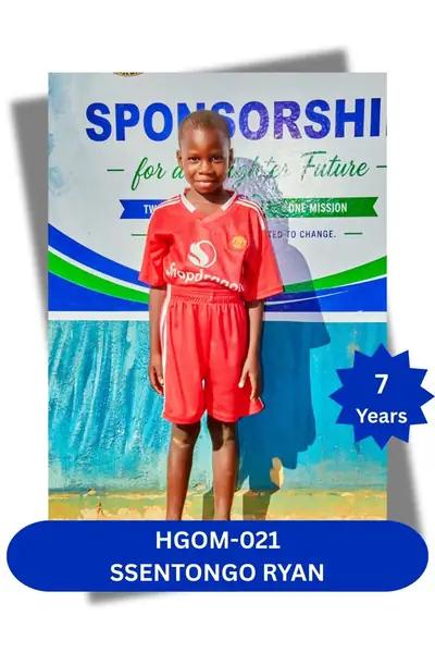 Boy in a red soccer jersey and shorts standing before a sponsorship banner