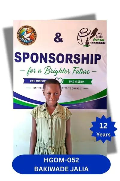 Girl in a sleeveless cream eyelet dress standing before a sponsorship banner