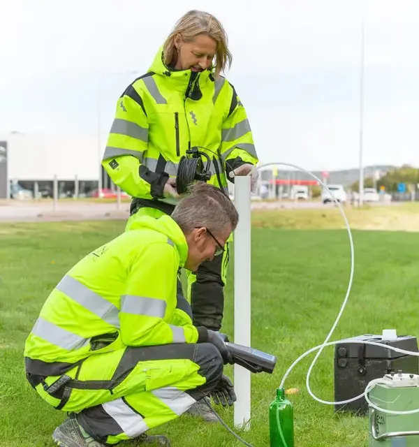 Två medarbetare tar grundvattenprov från ett rör i en gräsmatta