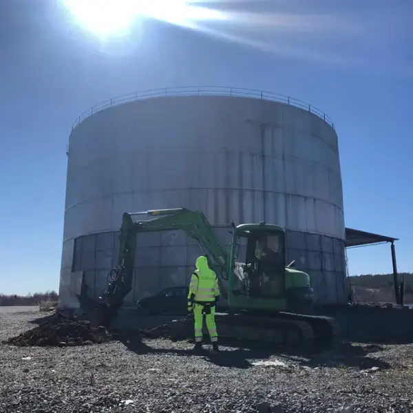 Medarbetare i varselkläder vid en grävmaskin framför en cistern