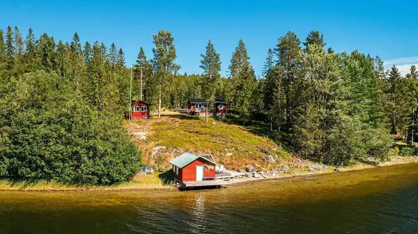 Röda stugor och en sjöbod på en skogsklädd strand vid vattnet