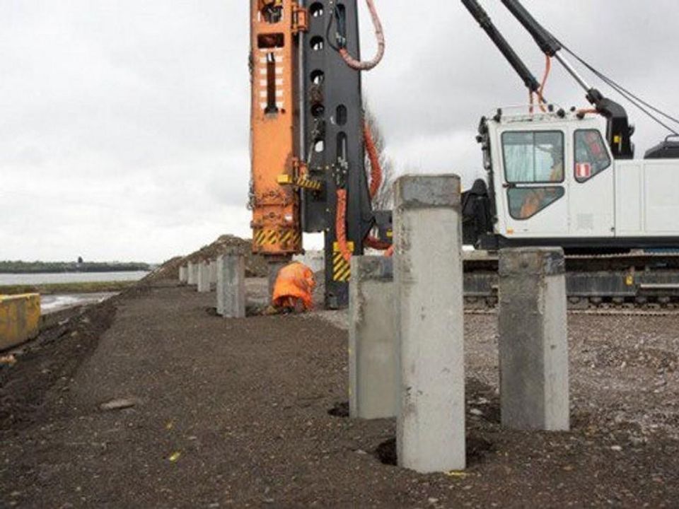 Precast concrete piles driven in a line alongside a crawler crane