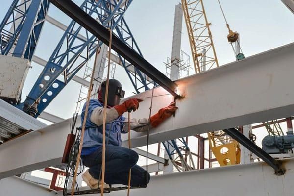 Welder joining structural steel members at height