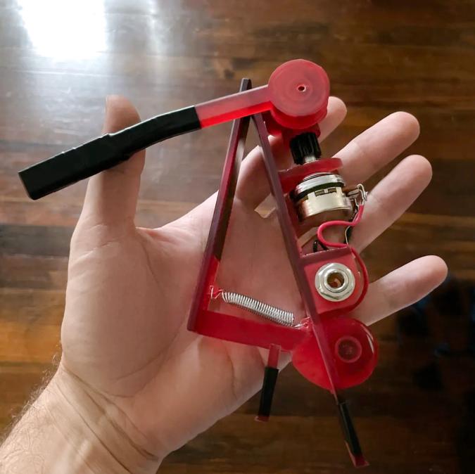 Image of the first prototype, a red clip on device with exposed electronics, in my hand