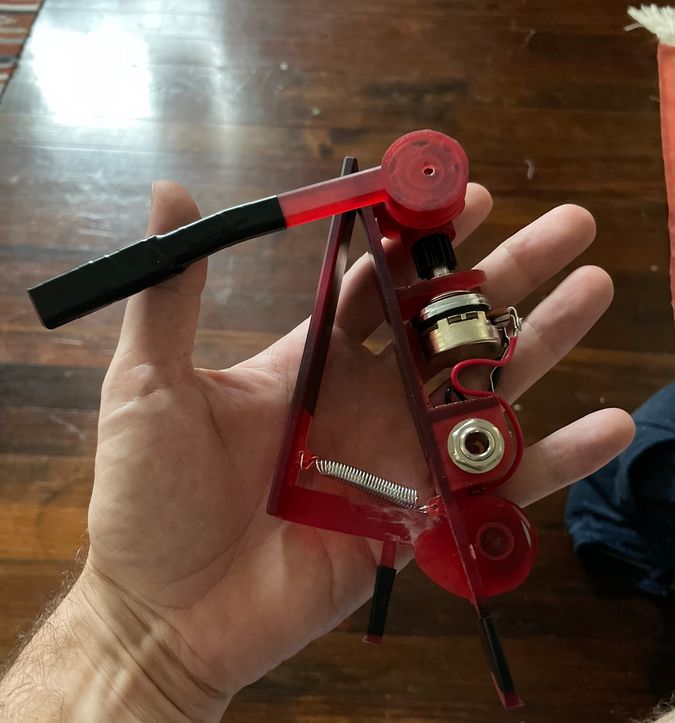 Image of the first prototype, a red clip on device with exposed electronics, in my hand