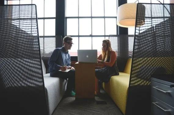 Two people sitting in a booth staring at a laptop