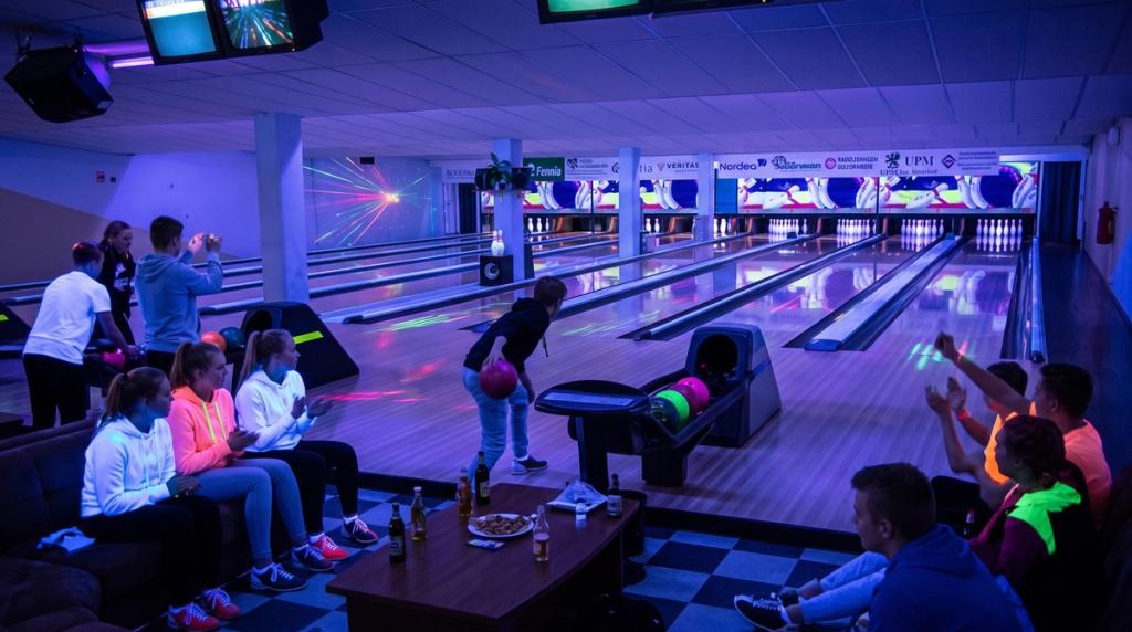 Glowbowlingkväll i UV-ljus: en bowlare kastar medan kompisarna hejar från soffan
