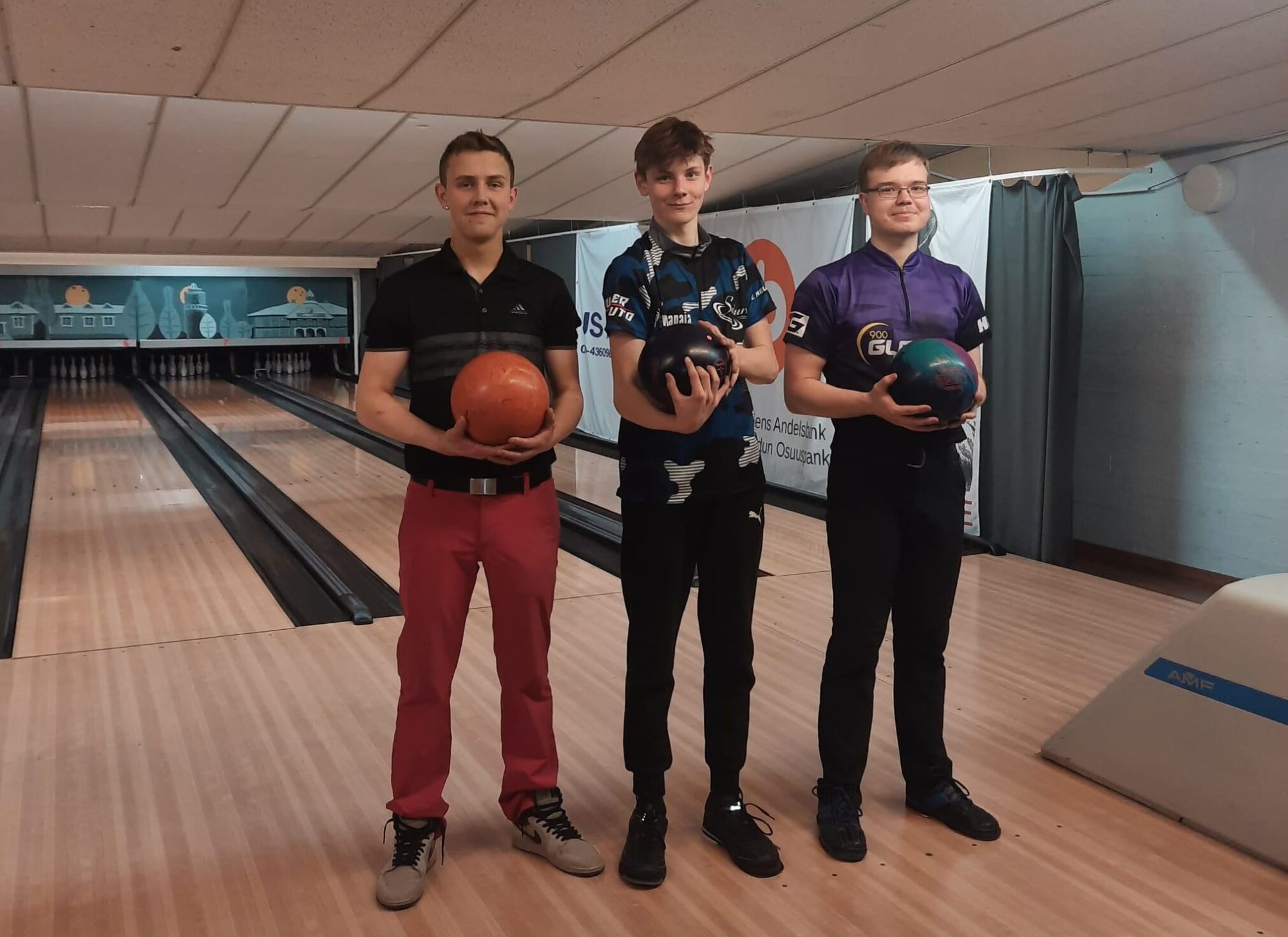 Tre bowlare med sina klot på banan, i bakgrunden målningen av Jakobstads gamla trähus