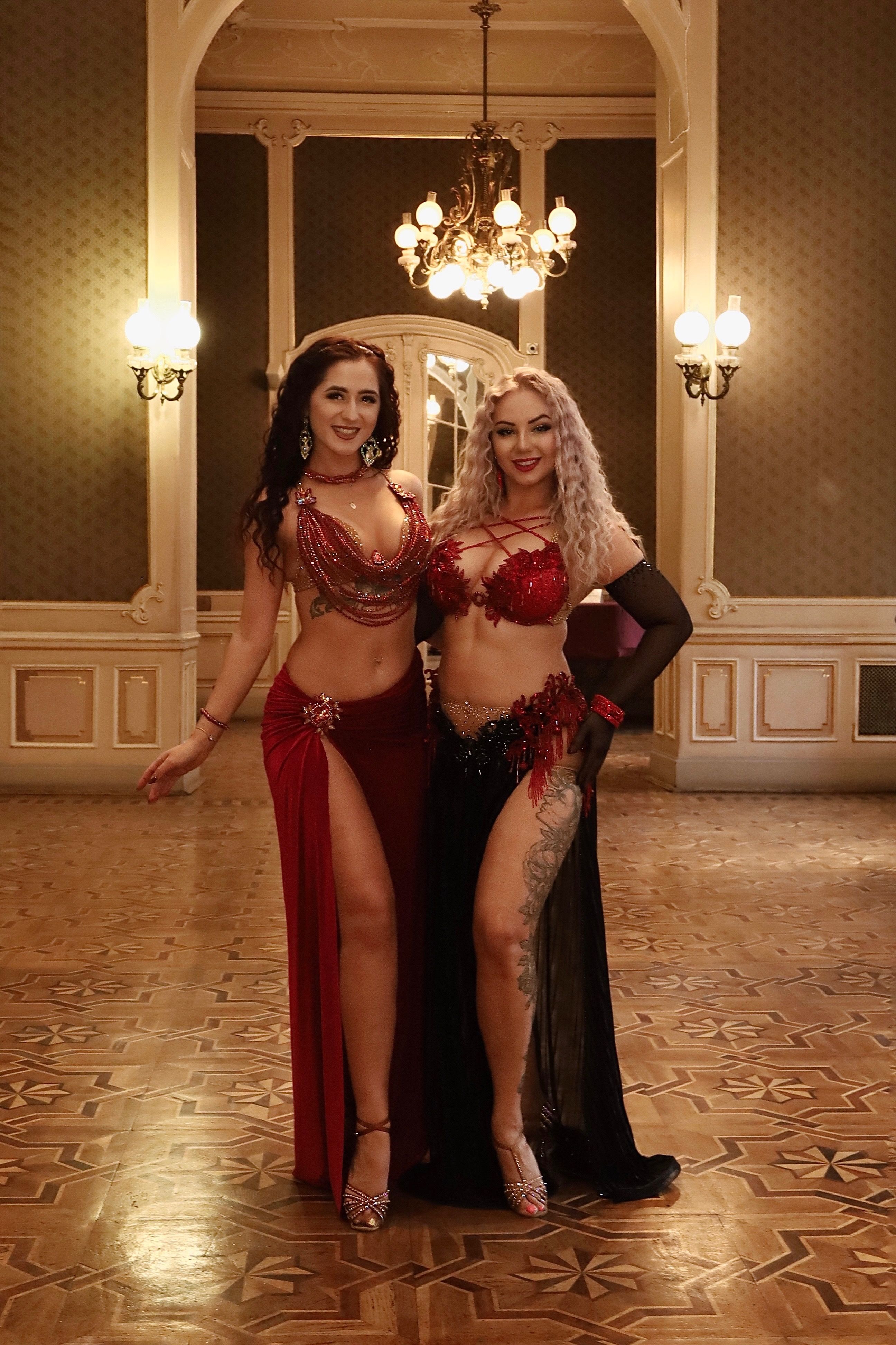 Duet tańca brzucha Wahatan w czerwonych strojach w eleganckiej sali balowej z żyrandolem
