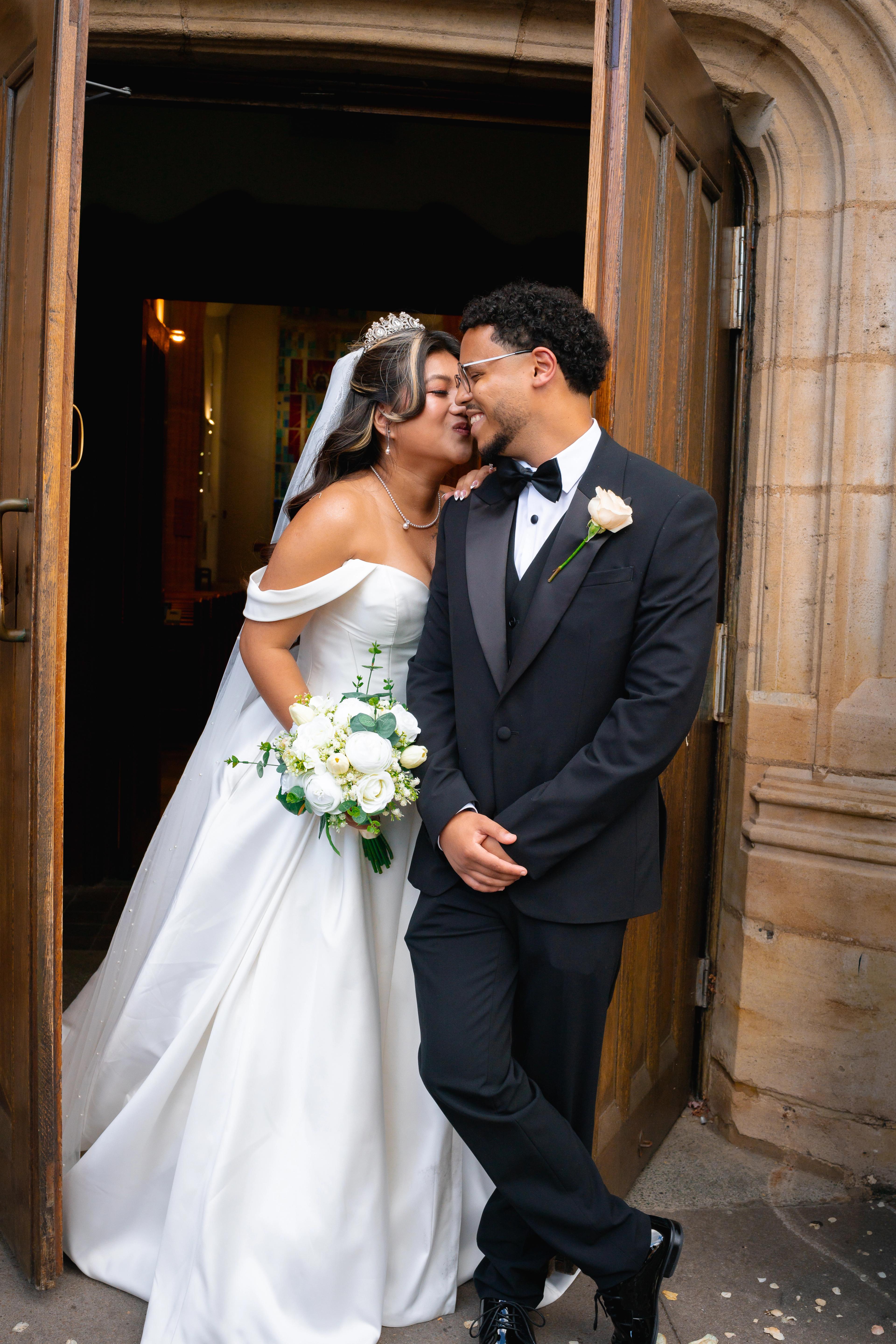 Bride and groom smiling at each other while standing in a church doorway.