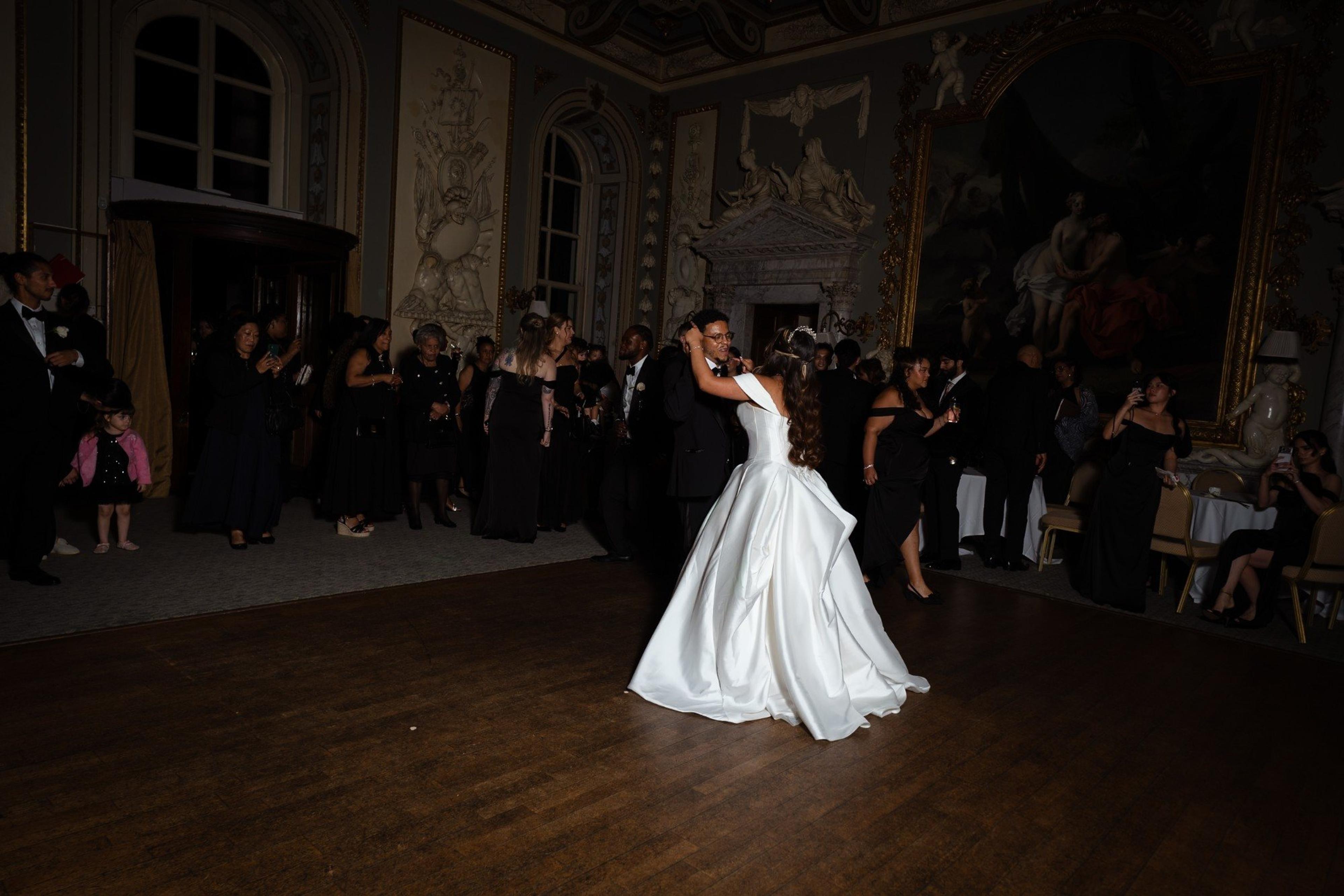 Bride and groom dancing in a candlelit ballroom while guests watch