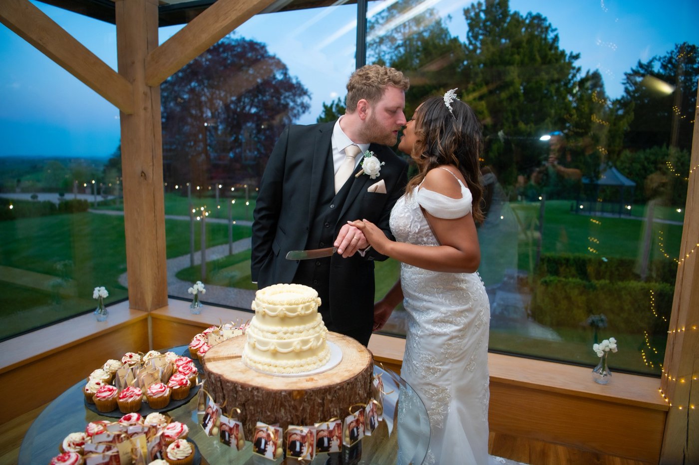 Nathan and Nastashia kiss as they cut their wedding cake in the Oak Barn at Bredenbury Court Barns