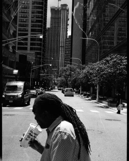 Man with dreadlocks sipping on a beverage in the middle of the street